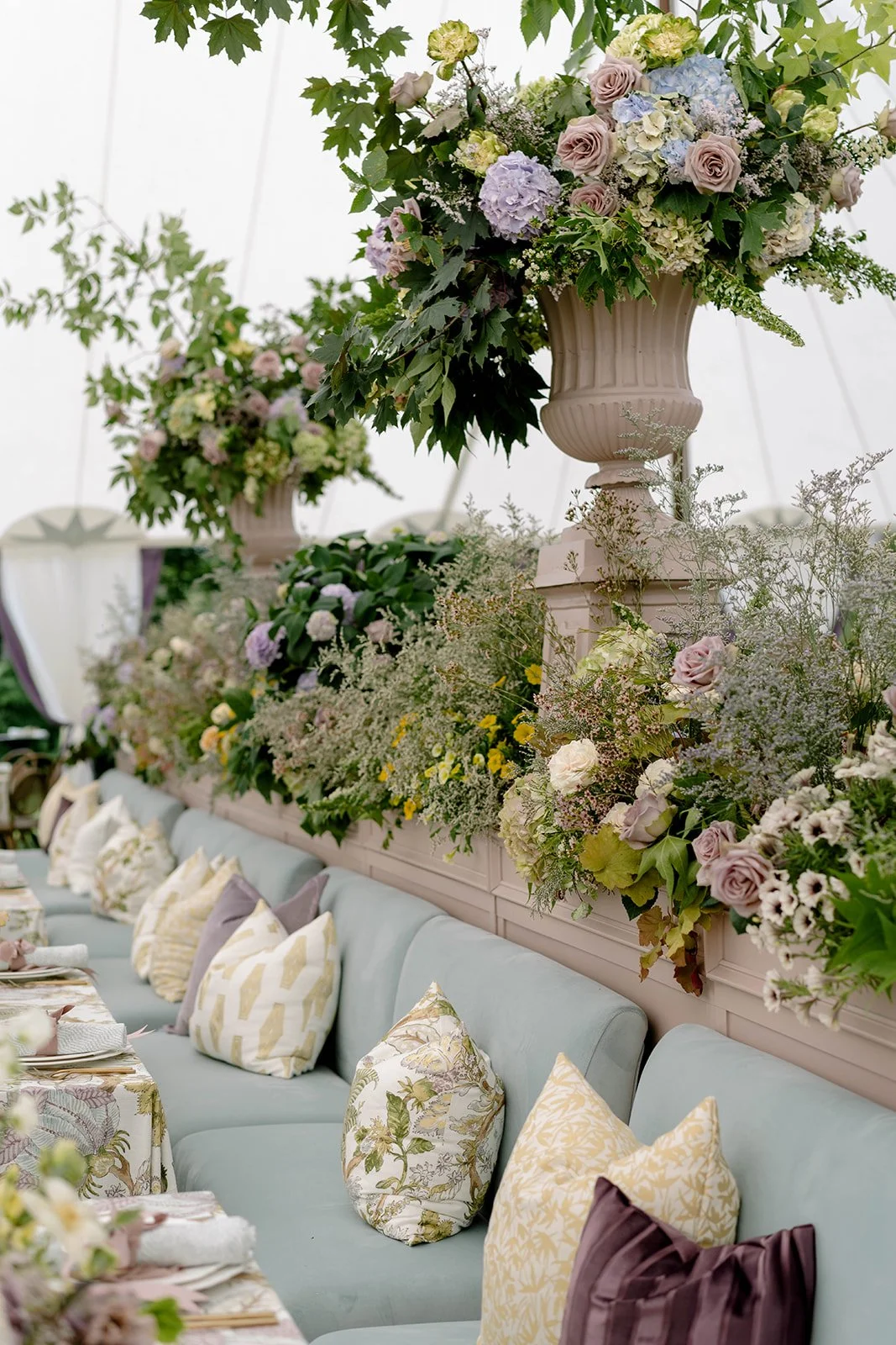 Elegant table setting with a pastel blue couch and an elaborate floral arrangement with pink, purple, and white flowers in large vases.