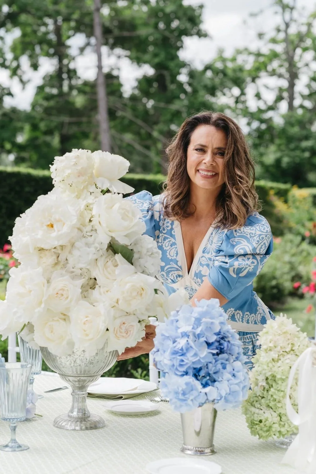 Woman arranging white and blue flower centerpieces at an outdoor table.