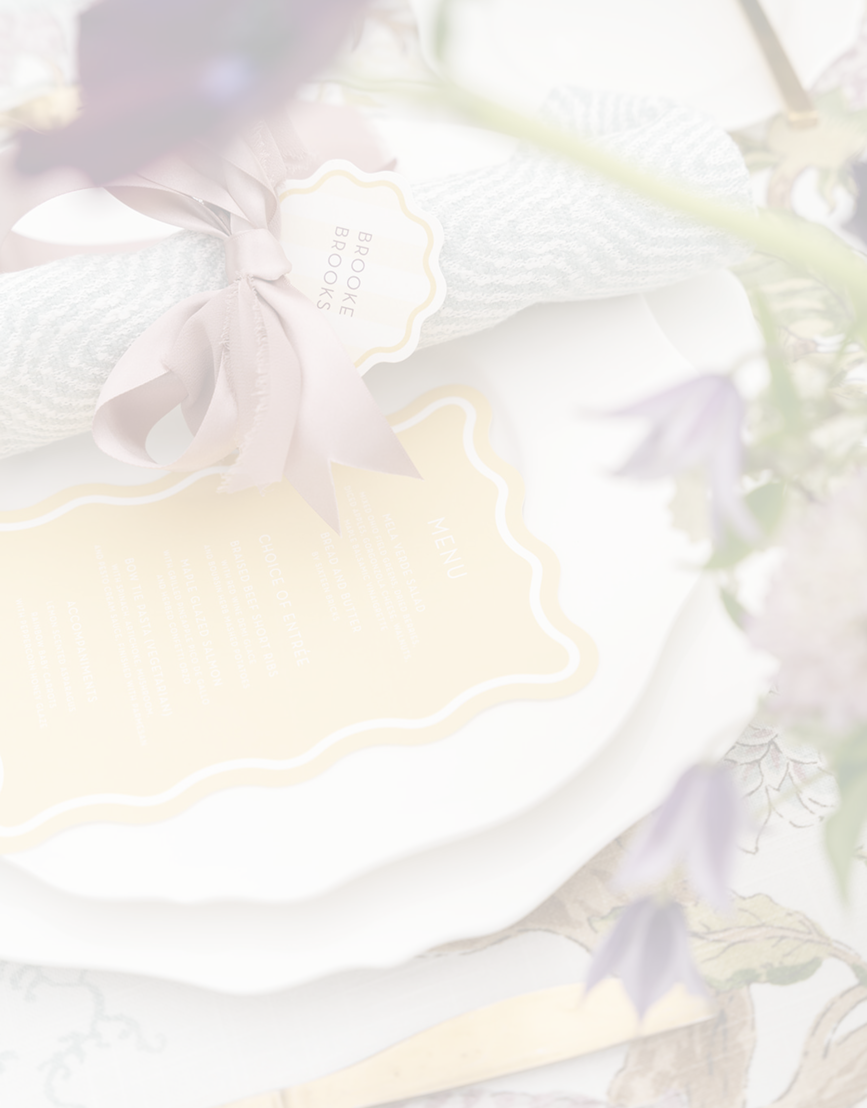 A gift wrapped with a light purple ribbon, labeled 'Breakfast Books', with a menu and decorative paper, surrounded by purple flowers.