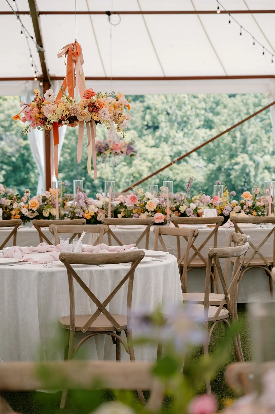A decorated event tent with floral arrangements and wooden chairs around tables, set for a celebration or wedding reception.
