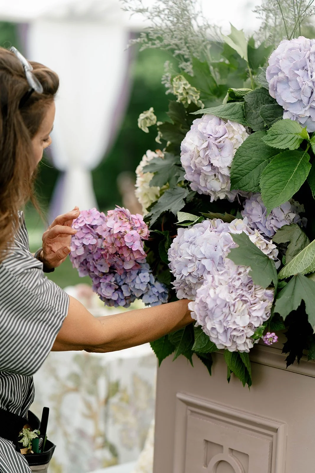 A woman arranging light purple and pink hydrangea flowers on a large floral display.