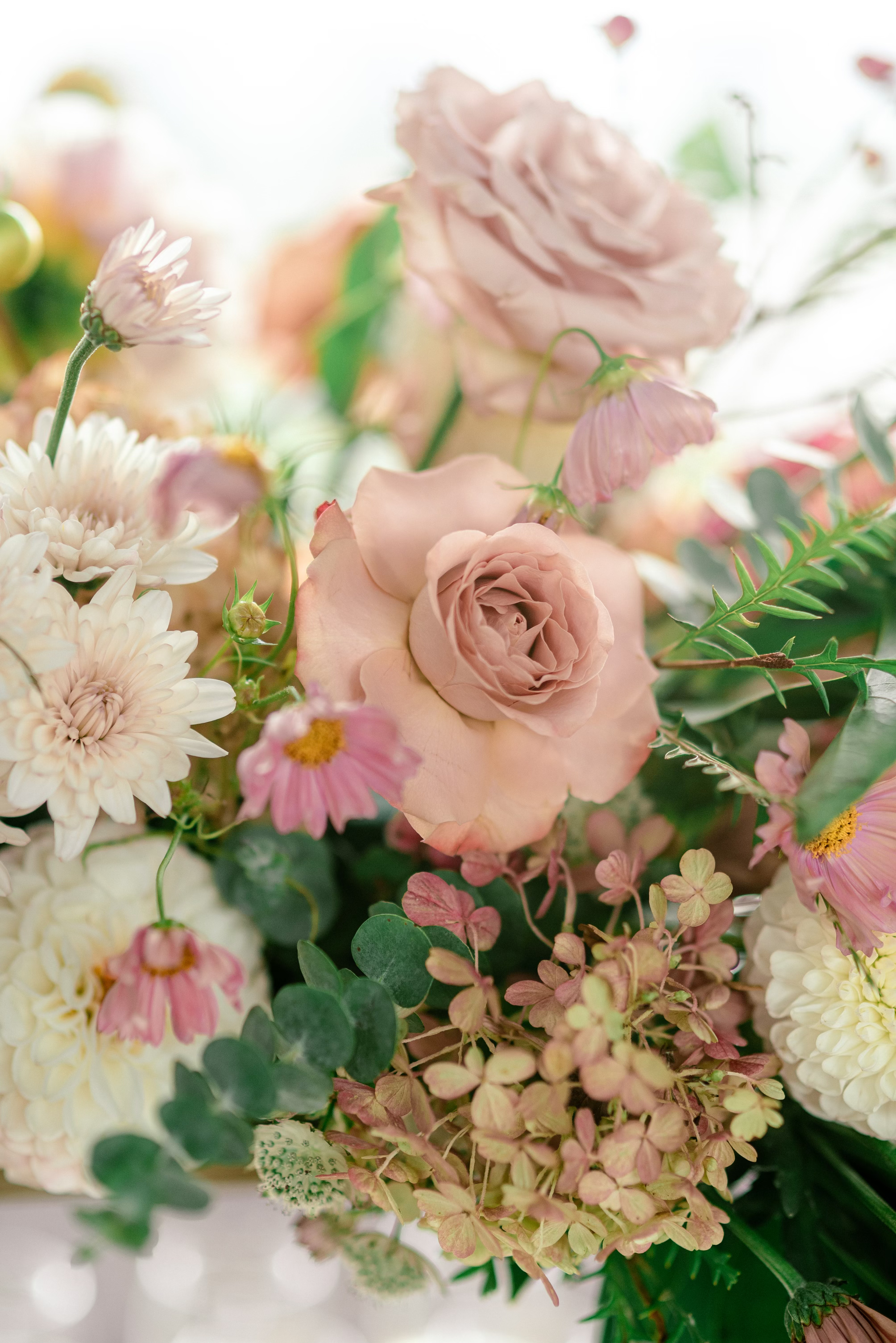 A close-up of a soft pink and white floral bouquet with roses, daisies, and greenery.