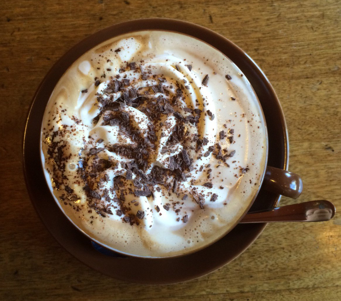 A cup of coffee with whipped cream and chocolate shavings, served on a wooden table.