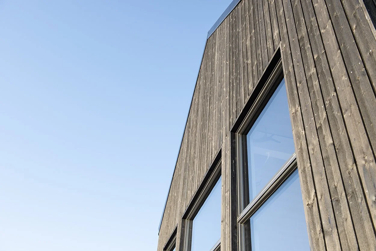 Close-up of a modern wooden building with large rectangular windows against a clear blue sky.