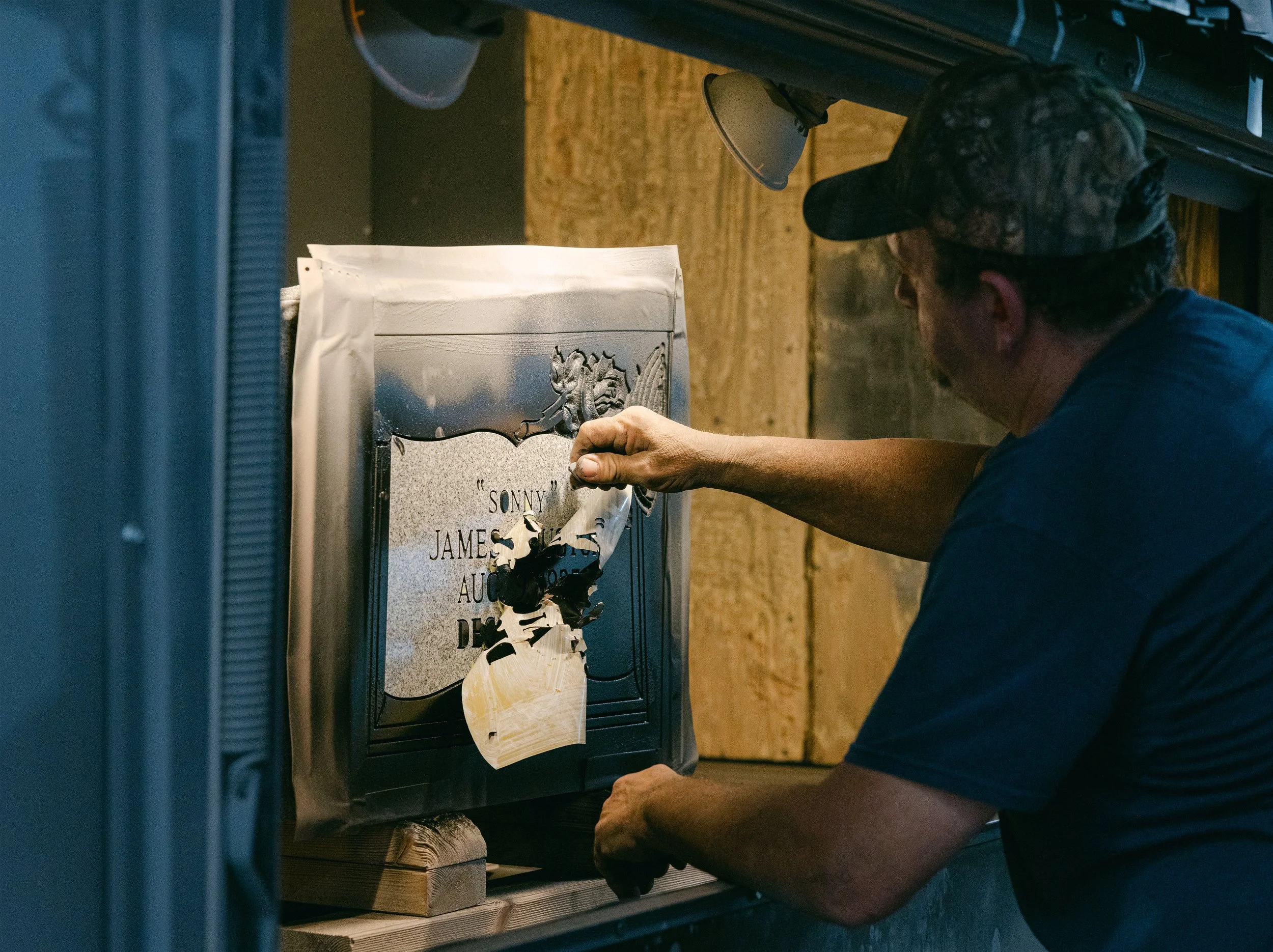 A man in a workshop peeling a stencil off to reveal the final design