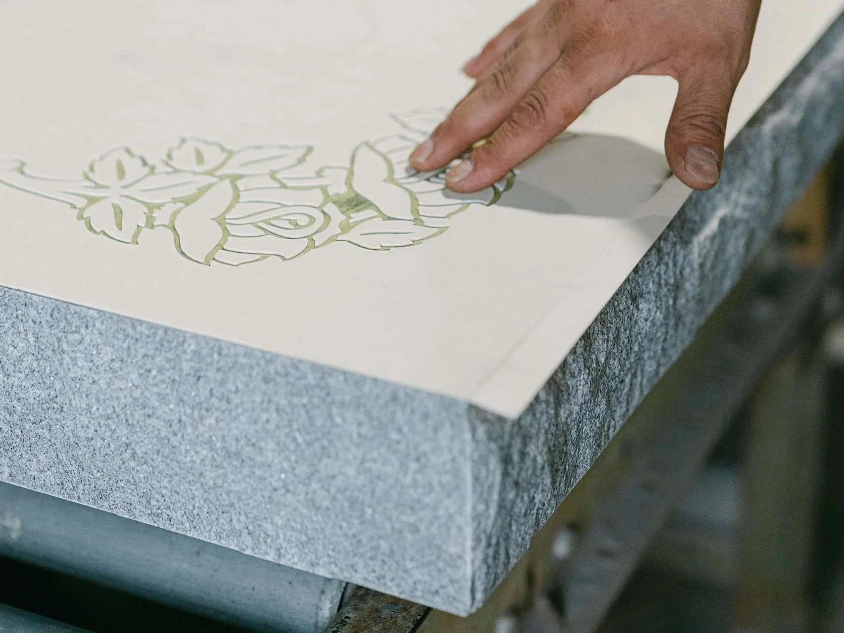 A man's hand feeling the cutouts of a ublast flowers stencil on granite