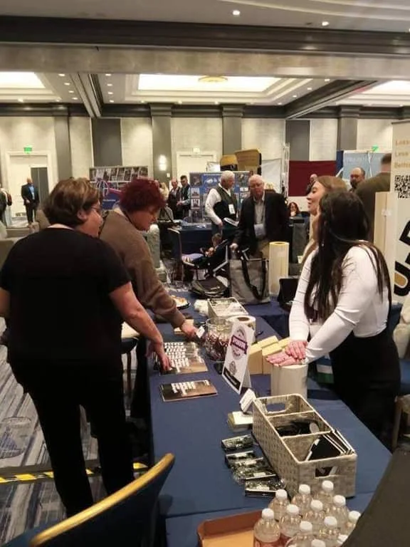 Four women at a tradeshow talking at a booth table about ublast