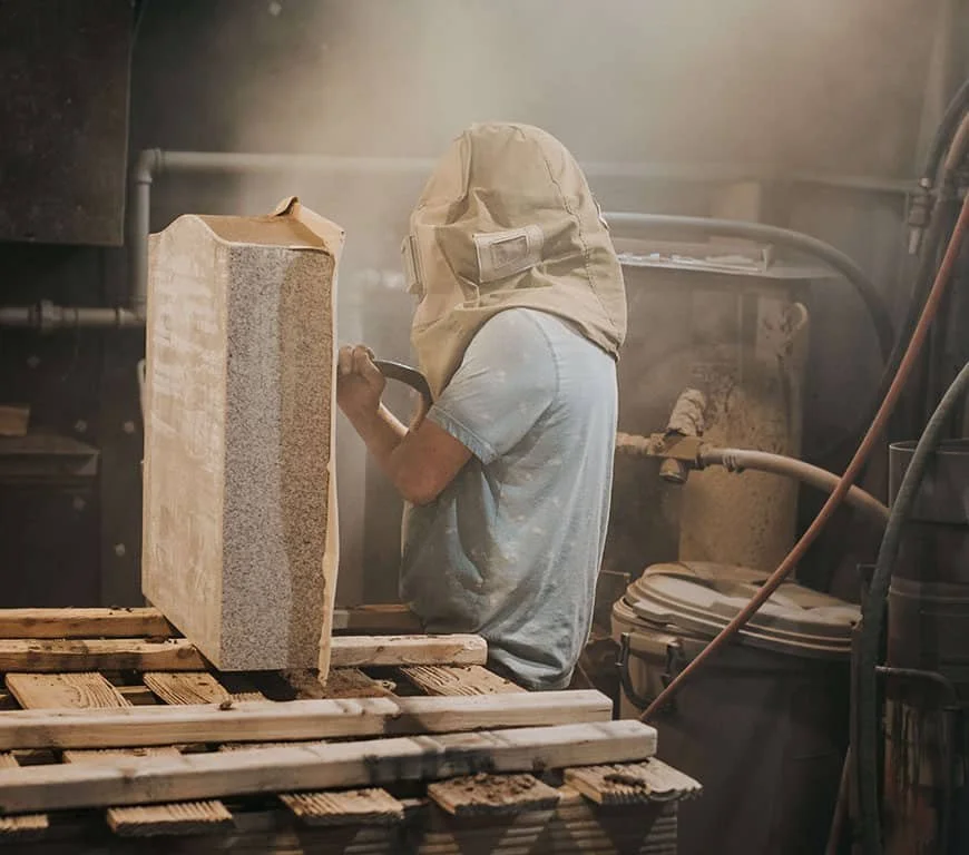 A man sandblasting a headstone with a headcovering on
