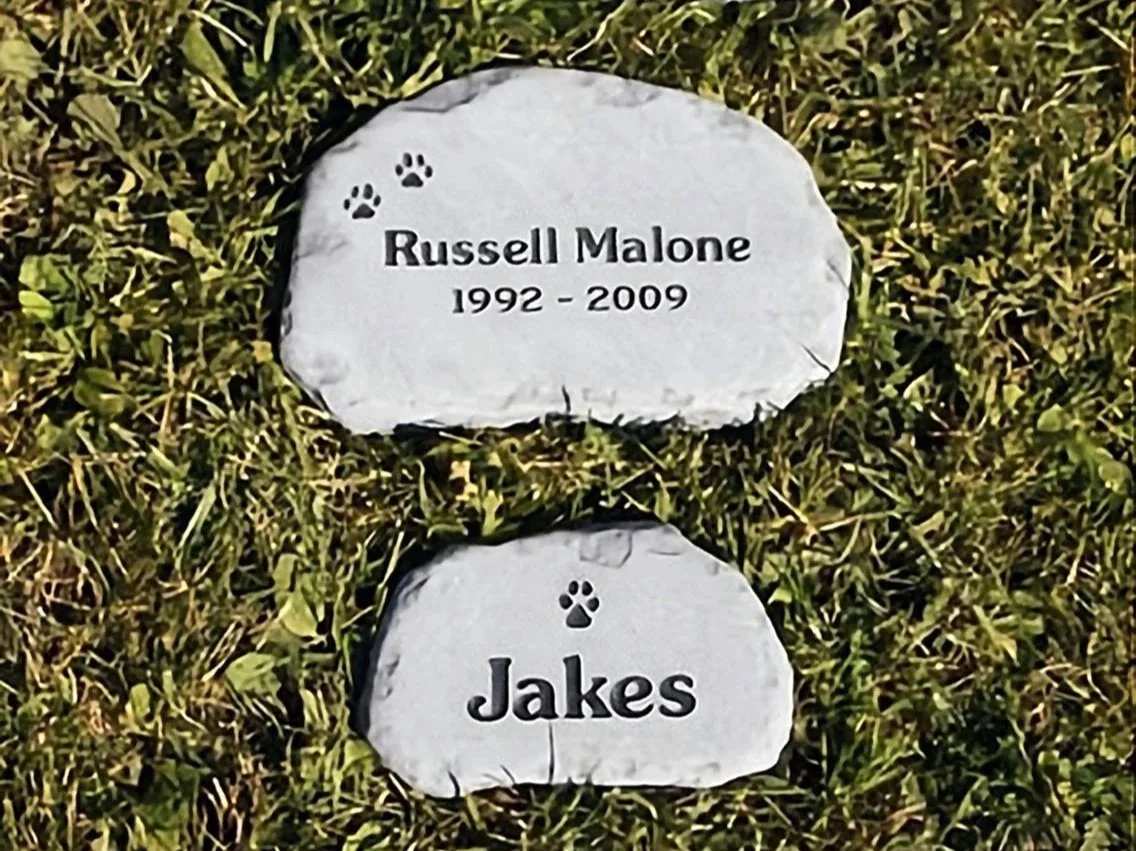 A photo of two pet memorial stones on the grass and stacked vertically with pet names and paw imprints