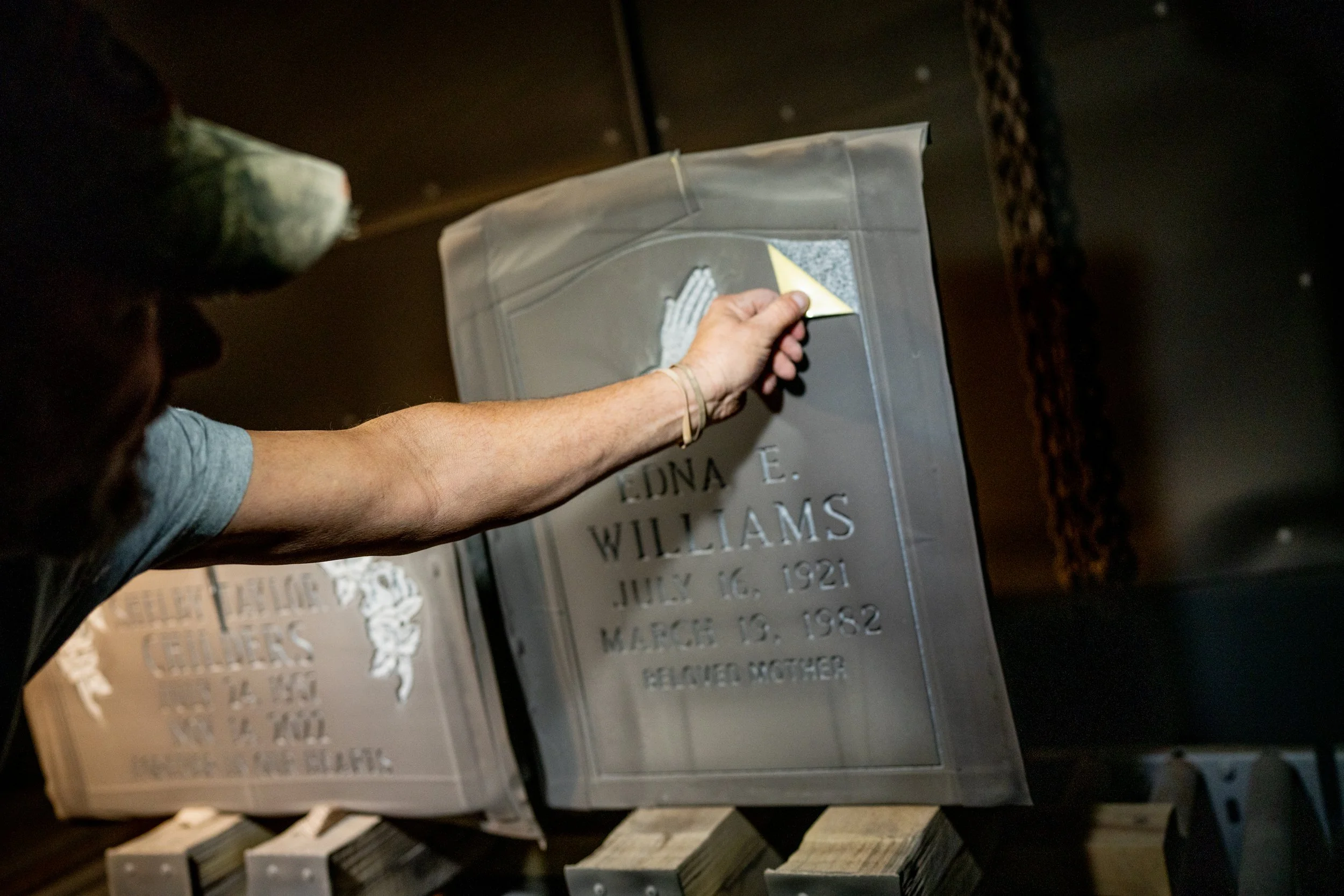 A man peeling a ublast stencil off of a granite headstone