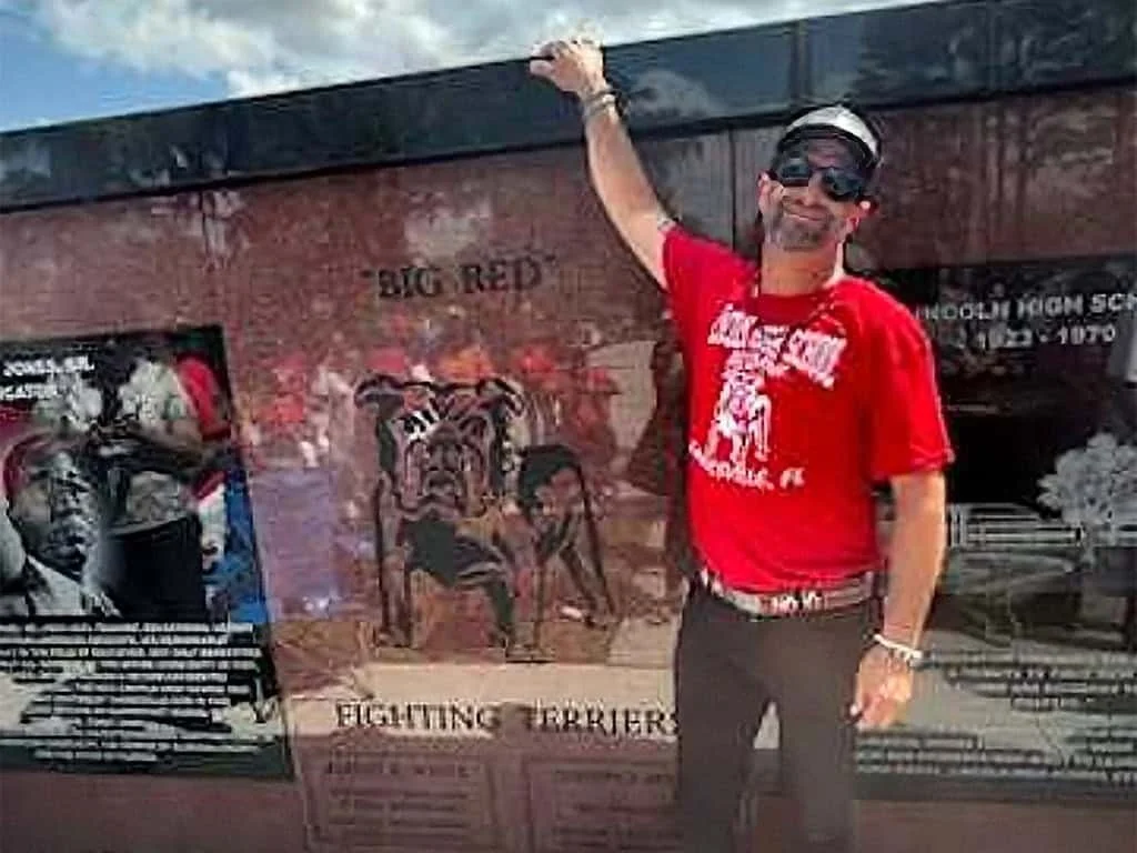 A man standing in front of a large brown and black memorial designed and built by ot davis
