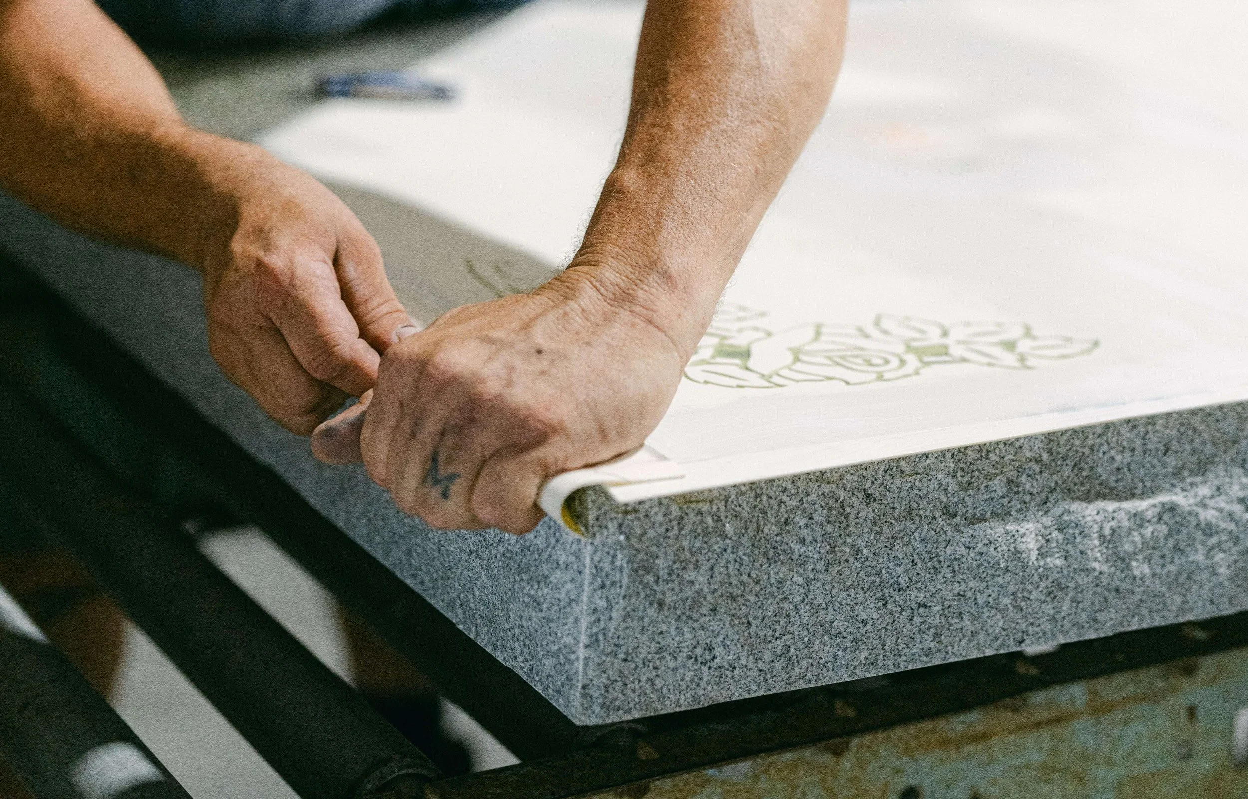 A closeup of a mans hands preparing the edges of a stencil on granite