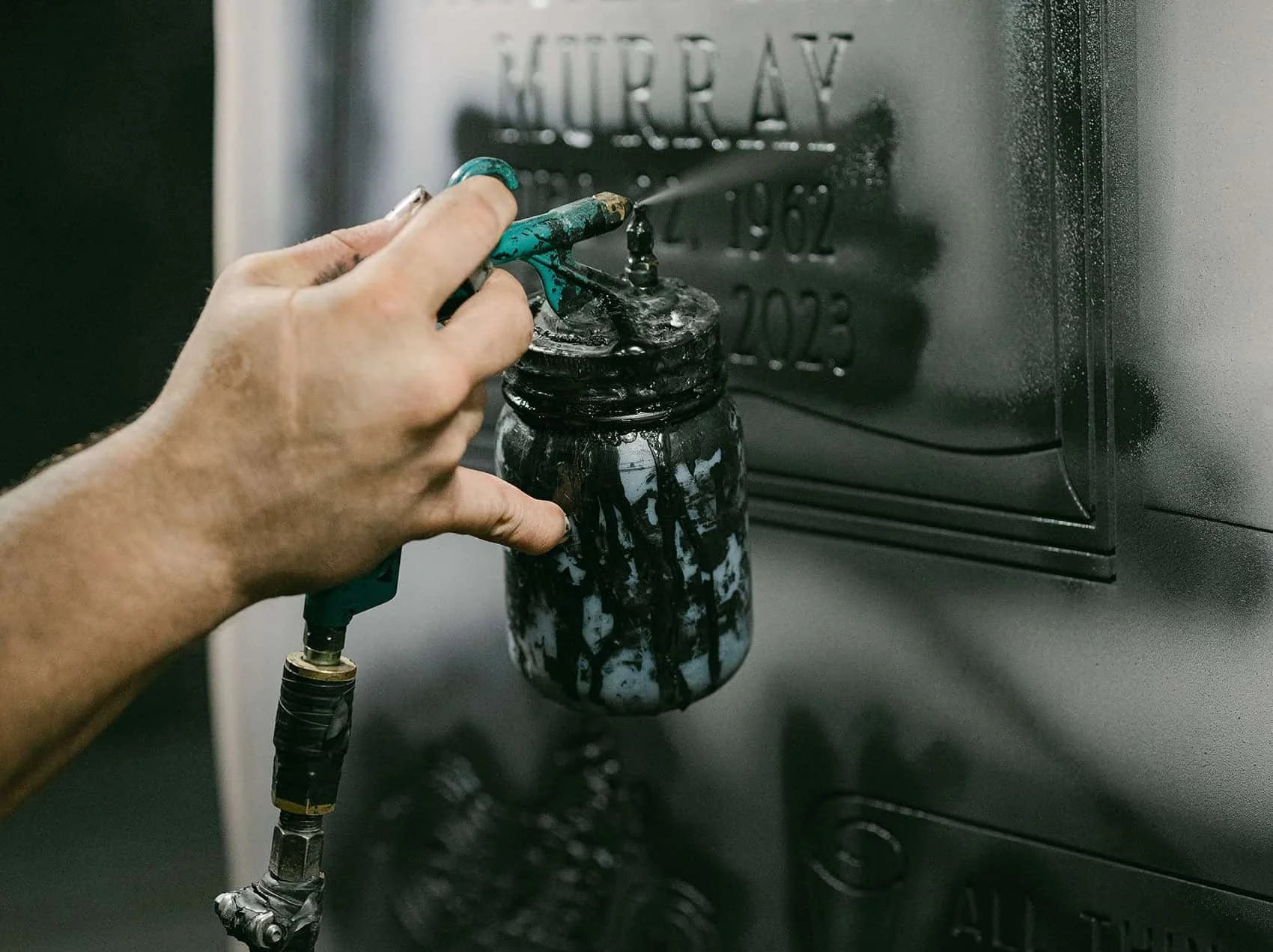A mans hand holding a spray canister to a headstone with a ublast stencil on it