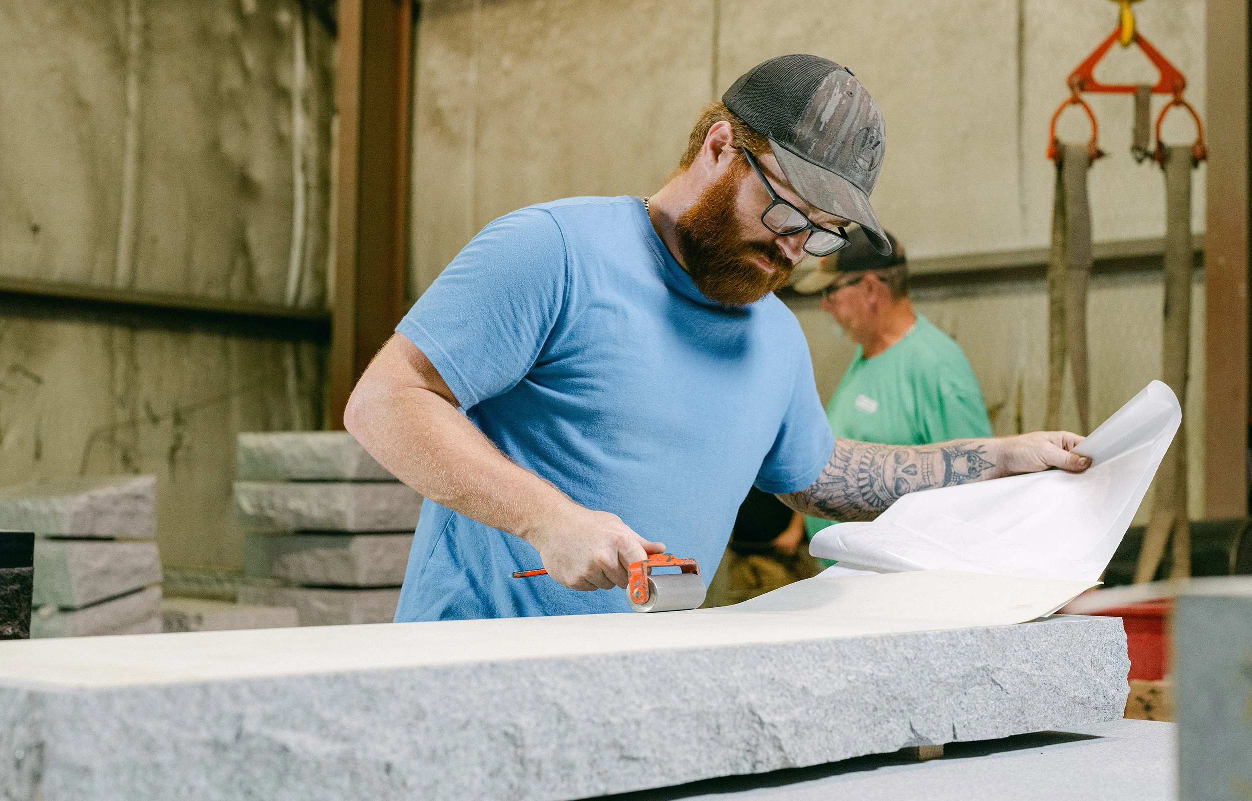 A man pressing a Ublast stencil onto a headstone with a roller