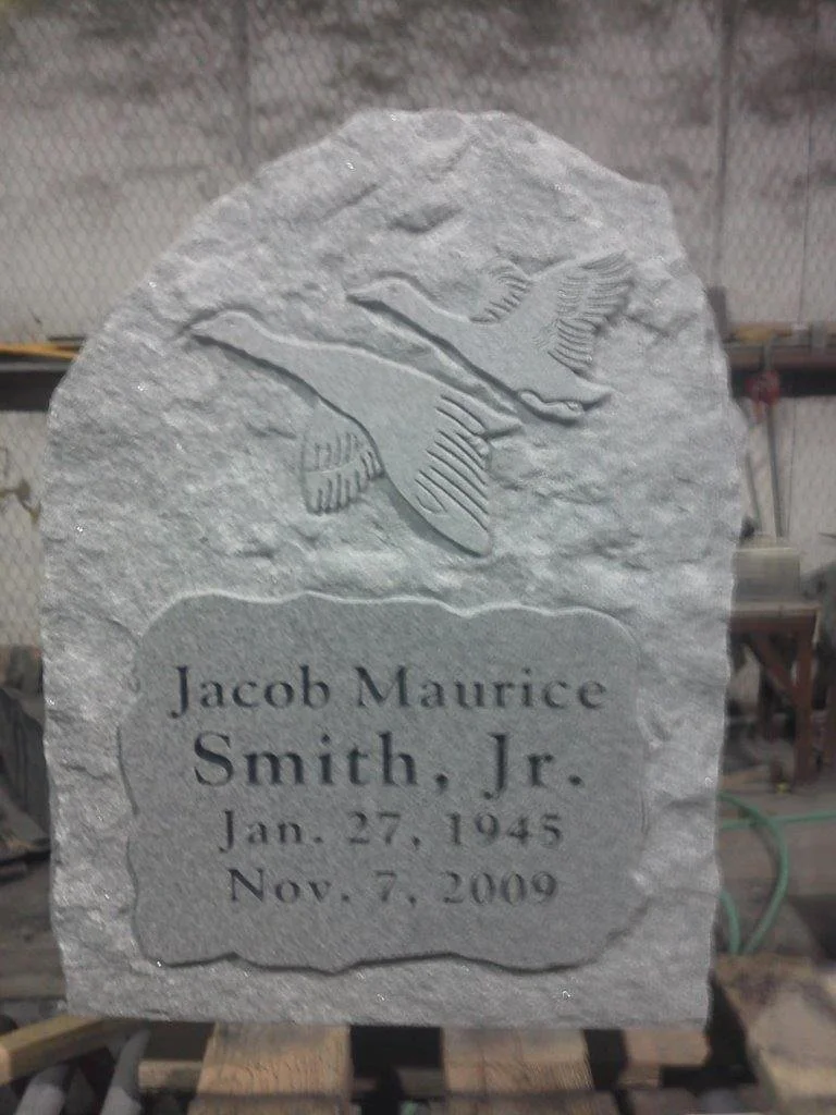 A gray stone memorial with an engraved image of two flying birds at the top and inscribed text that reads: Jacob Maurice Smith Jr., Jan. 27, 1945 - Nov. 7, 2009.