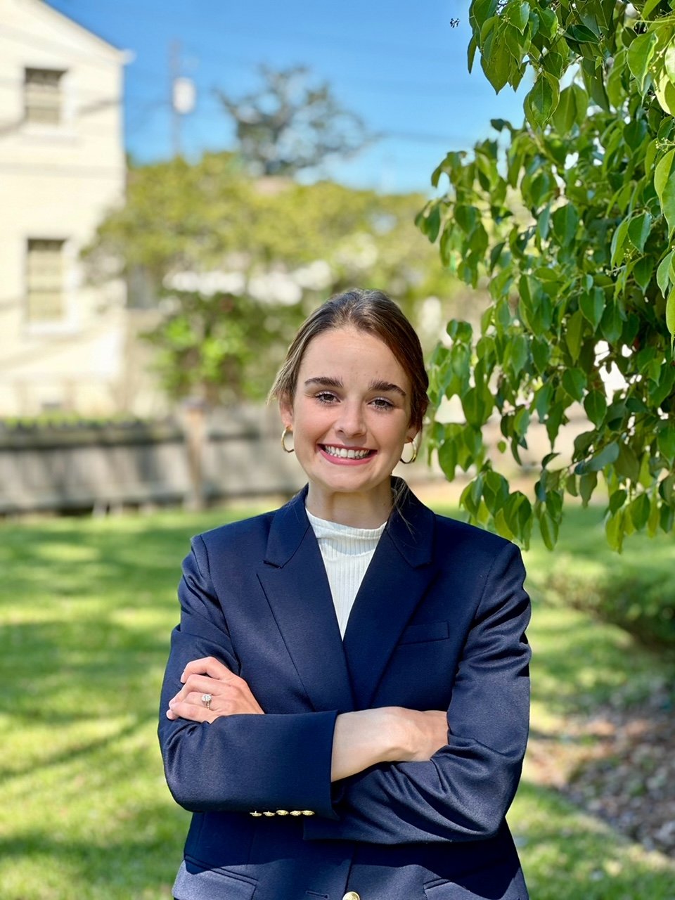 A female in a blue suit with a white shirt, smiling.