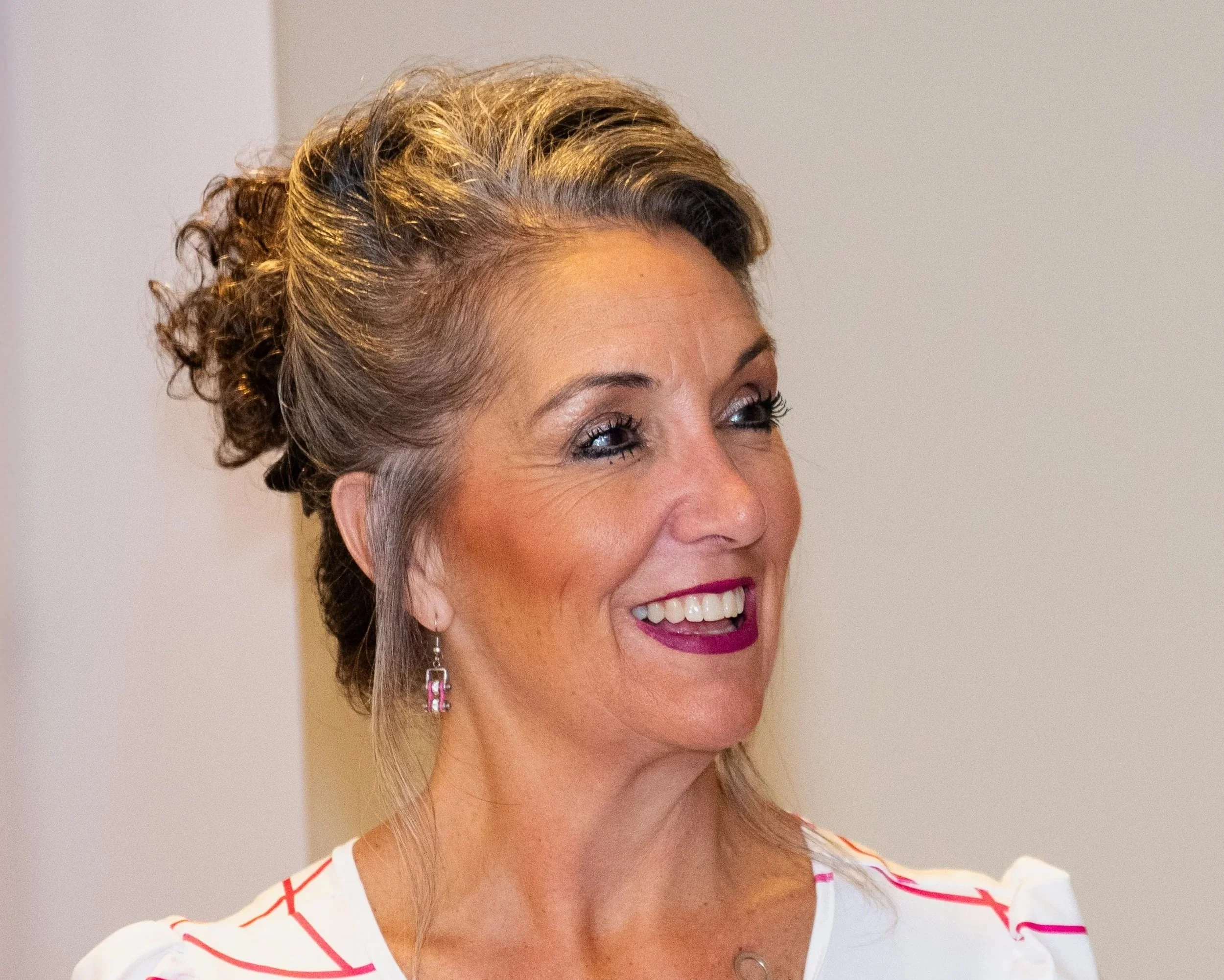 A smiling woman with short curly black hair wearing glasses, earrings, necklaces, and a striped shirt.