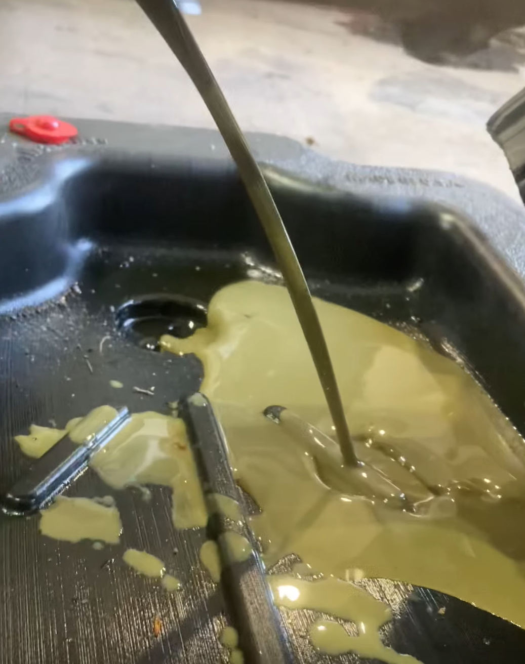 Milky, discolored engine oil draining into a pan during snowbike maintenance.
