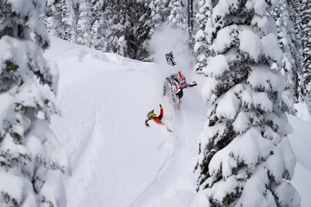 Rider beside an overturned snowbike in deep powder