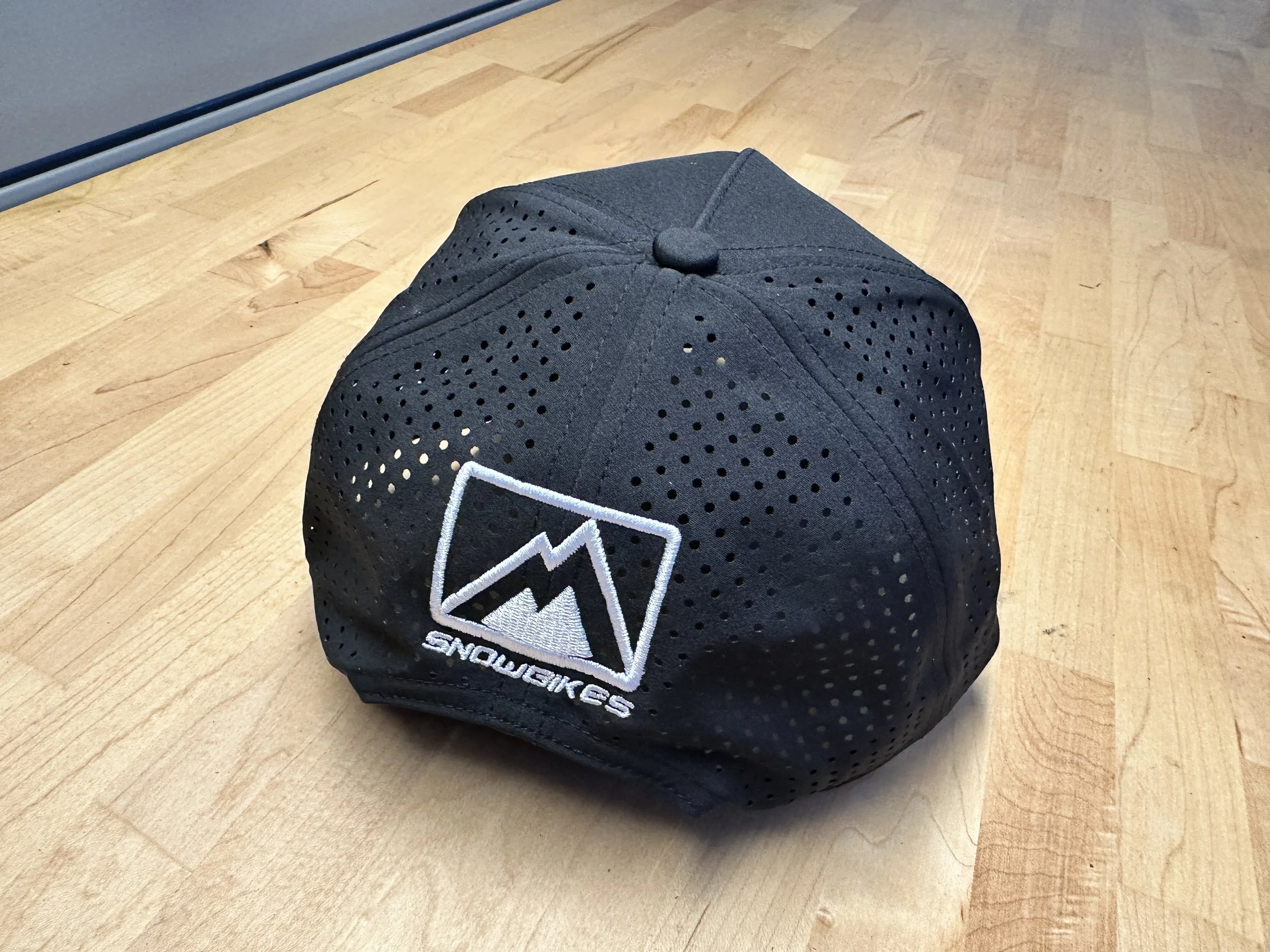 White MtnTop Snowbikes embroidery on the perforated back of the black Moto365 performance snapback.