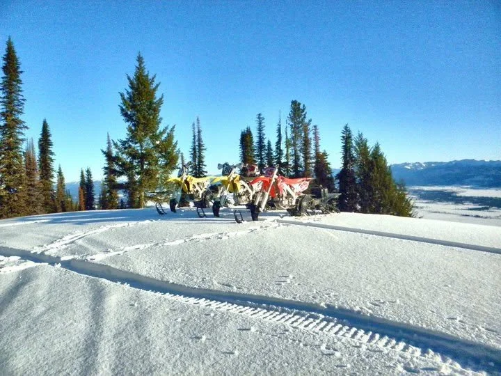 Three early snowbike conversions parked on a snowy mountain trail