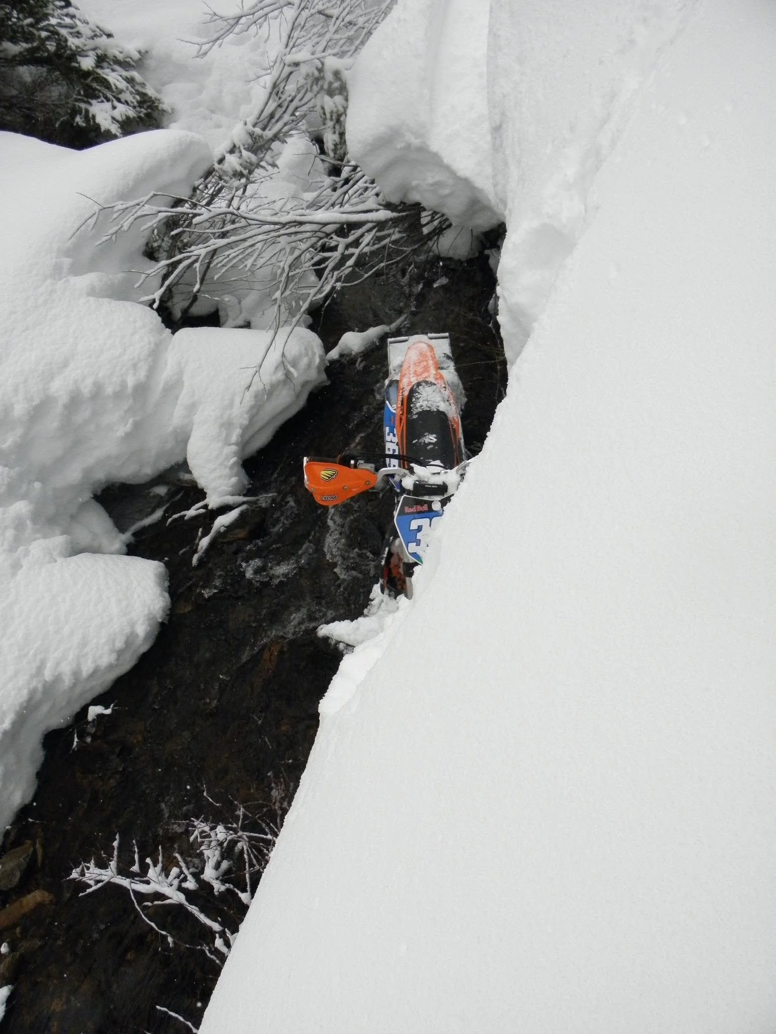 Snowbike lodged in an open creek between deep snowbanks.