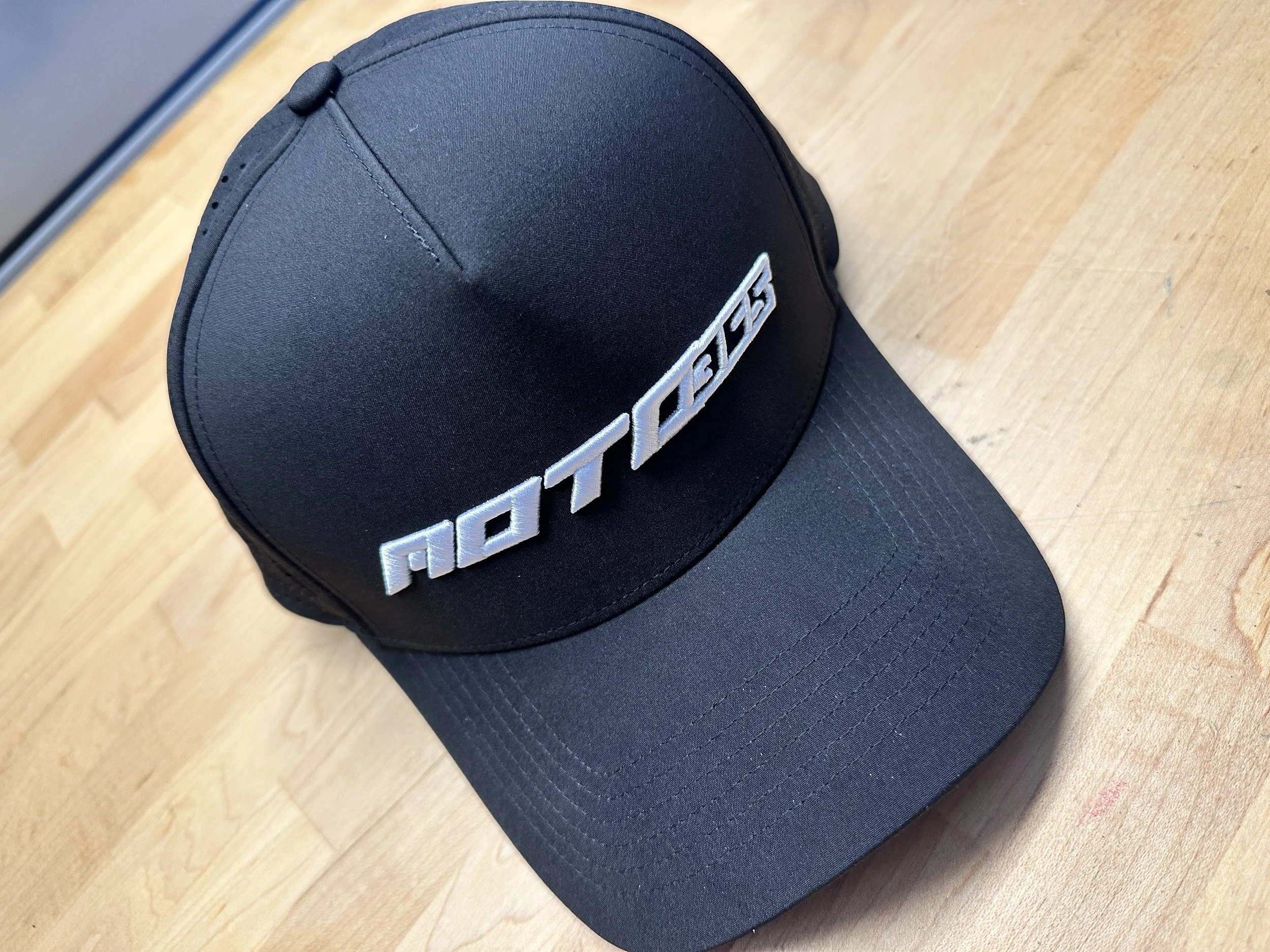 Close-up of raised white Moto365 embroidery and the curved bill on the black performance snapback.