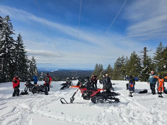 Group of snowbike riders gathered with their bikes under a blue winter sky