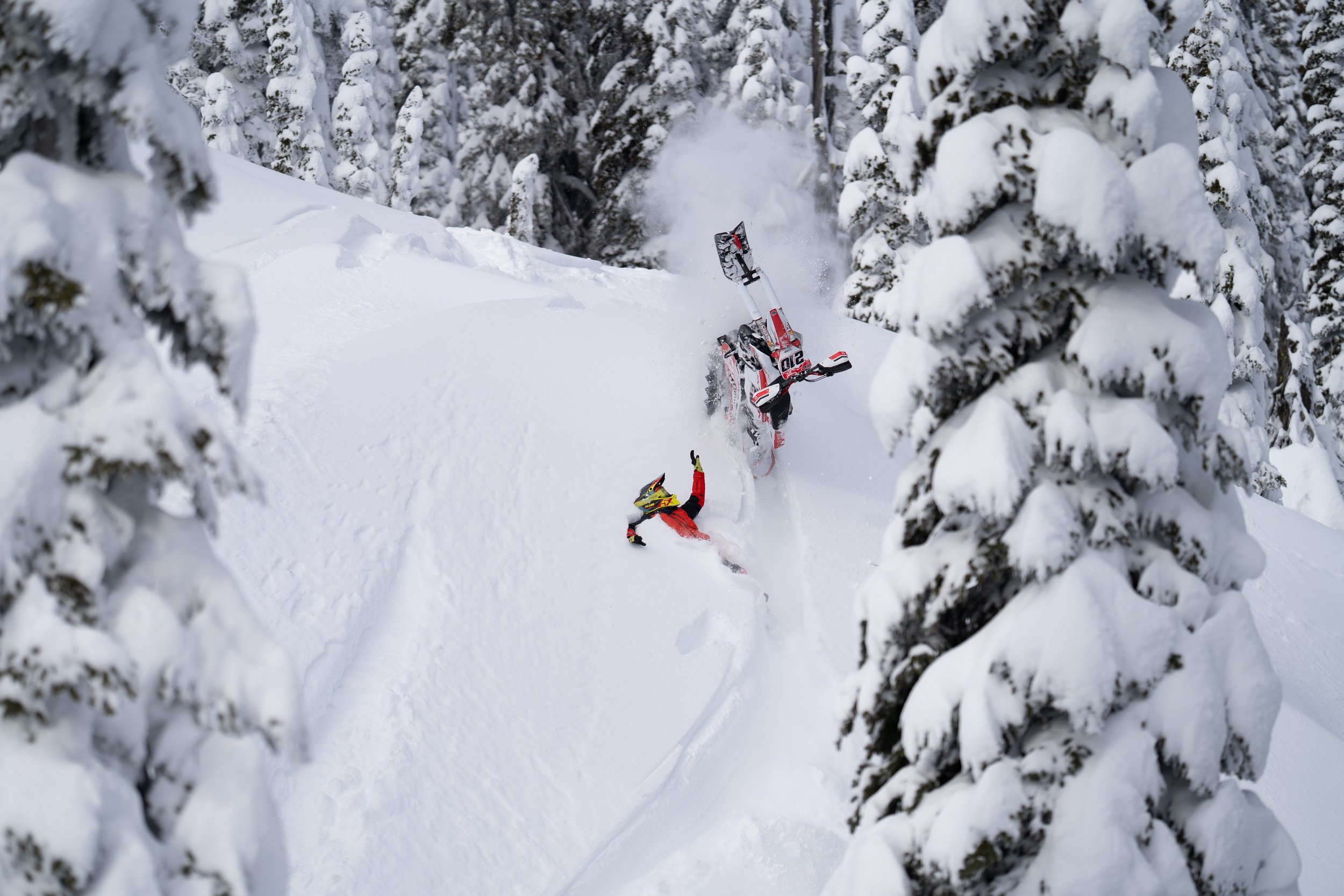 Rider beside an overturned snowbike in deep powder
