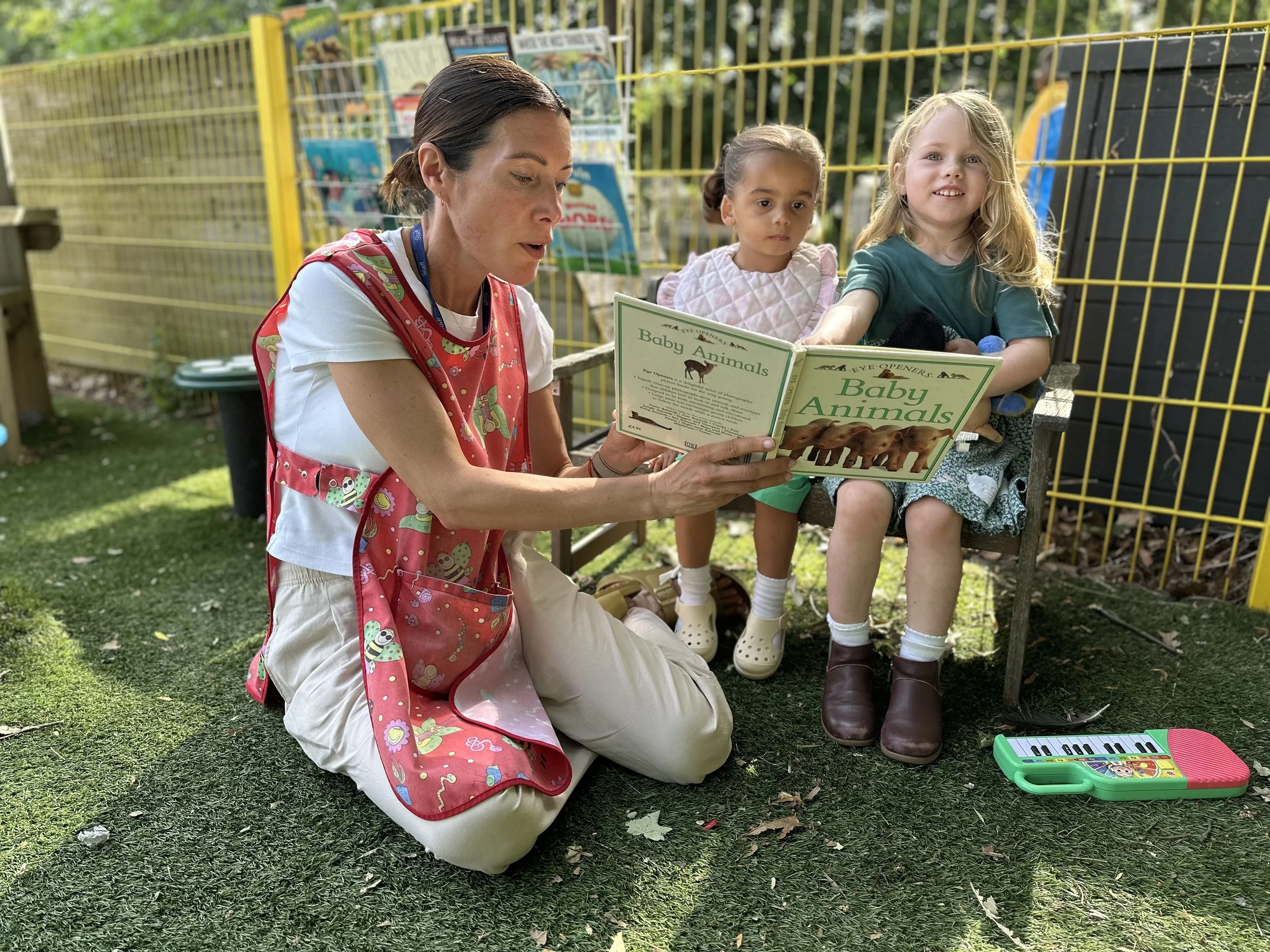 Sara-pre-school-practitioner-reading-book-with-nursery-children-outdoors-sidcup.jpeg
