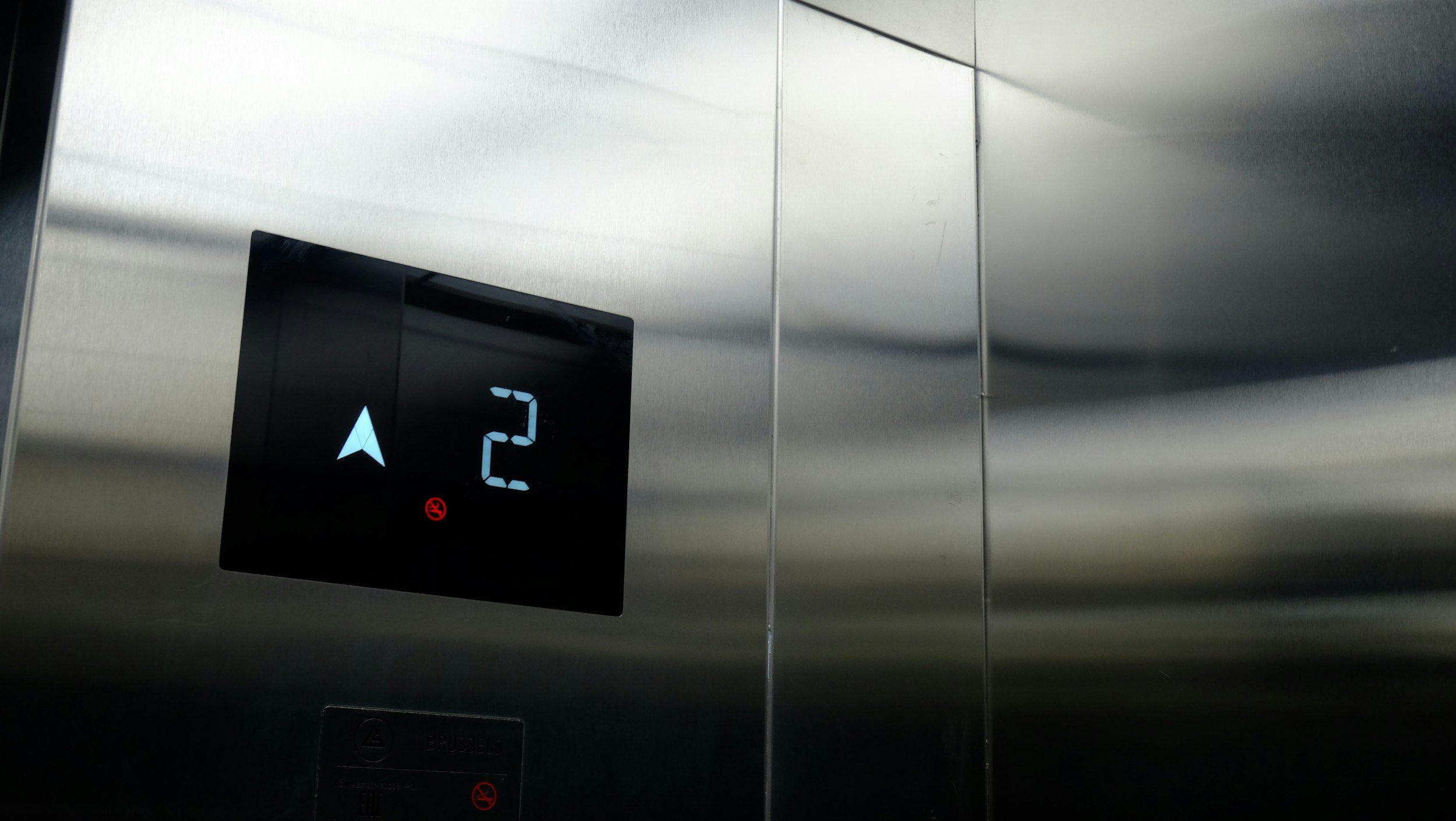 Elevator control panel displaying the number 2, with an arrow pointing upward, in a metallic elevator interior.