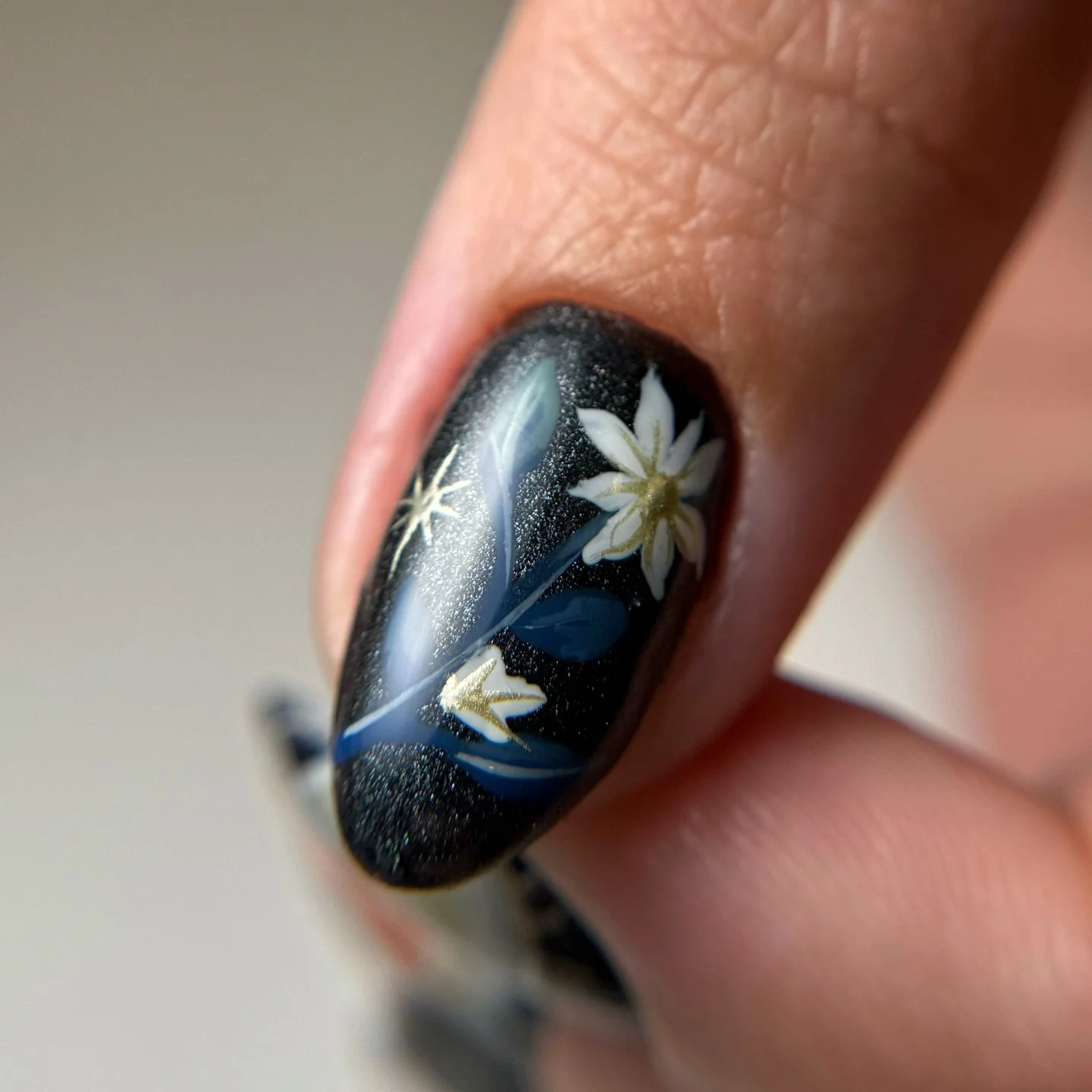 Close-up of a fingernail with black nail polish and white floral design.