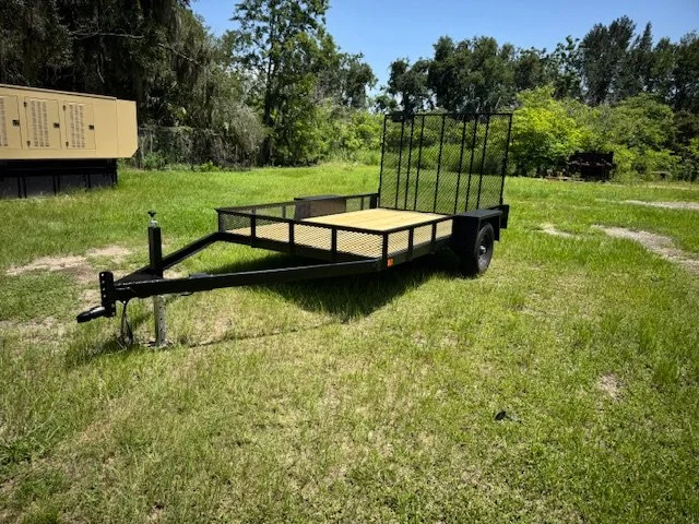 Black flatbed utility trailer with a ramp gate parked on grass
