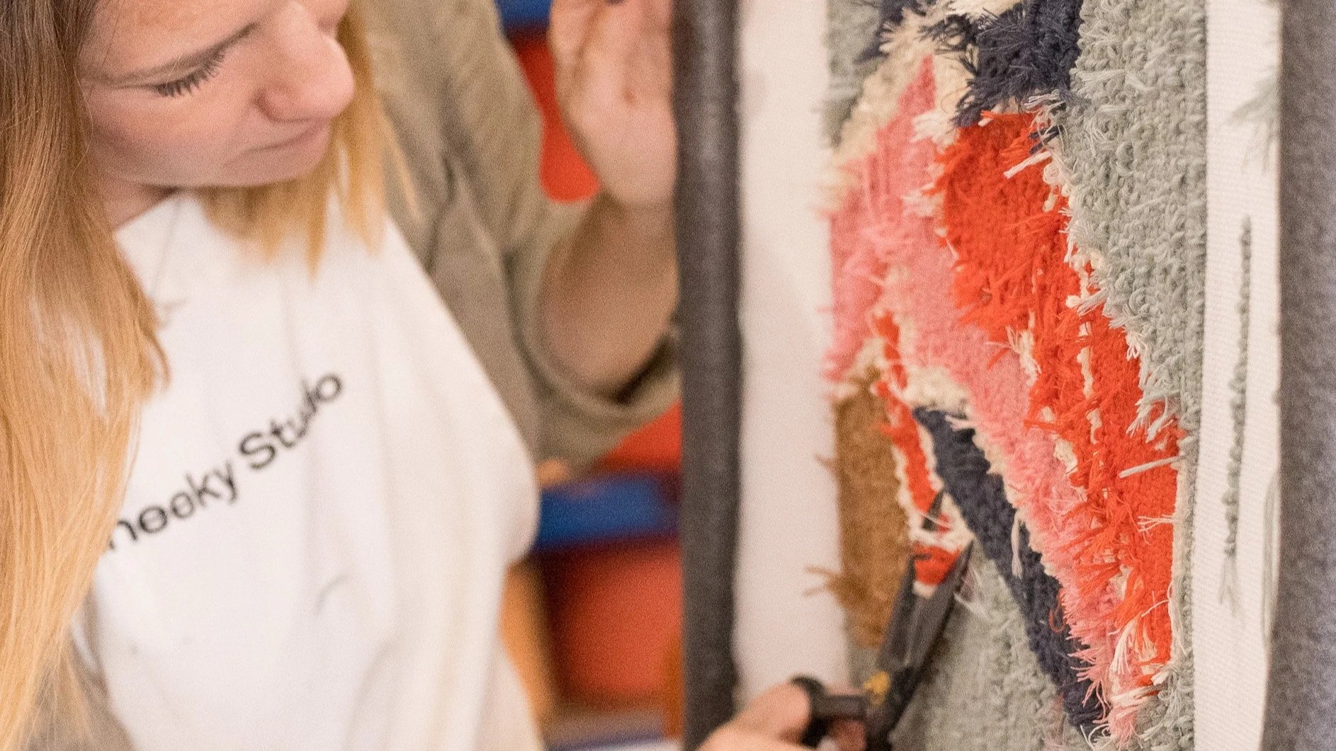 Woman examining a colorful shaggy rug displayed on a wall, holding a remote control or testing device.