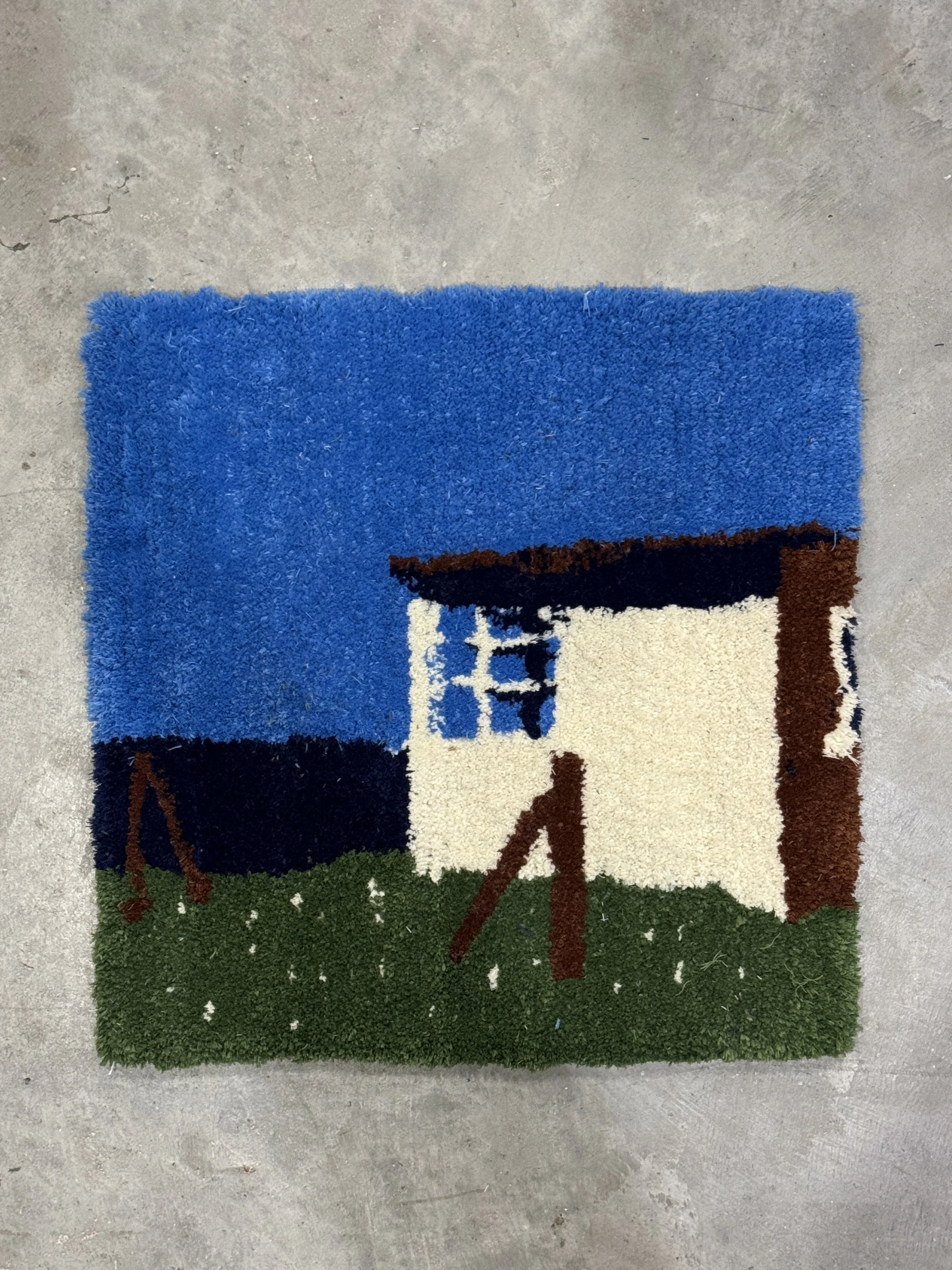 Colorful rug with a design of a house and swing on a green lawn, under a blue sky.