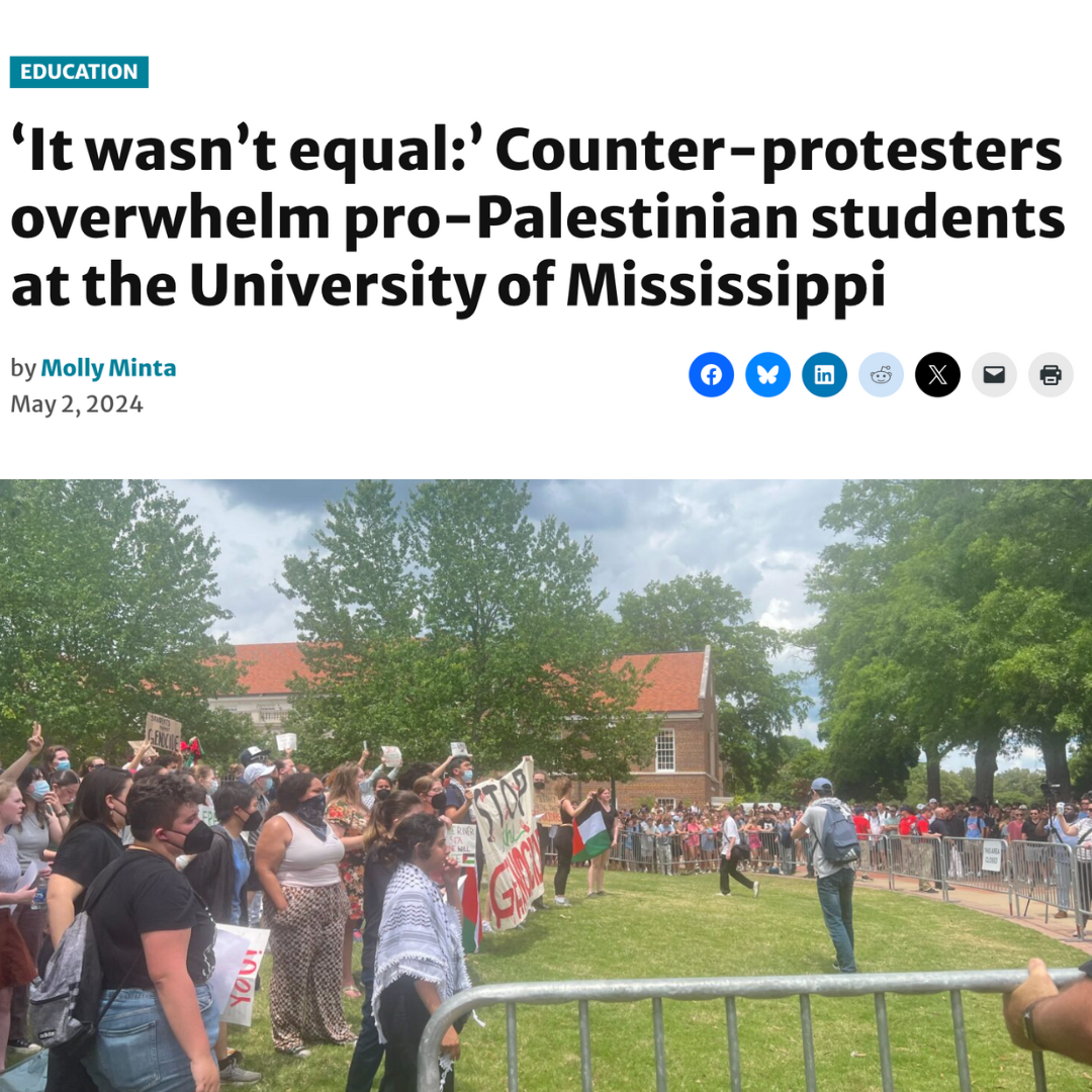 A crowd of pro-Palestinian students stands behind barricades, holding signs like “Stop the Genocide” during a campus protest. A larger group of counter-protesters is visible across the lawn. A photographer captures the tense scene.