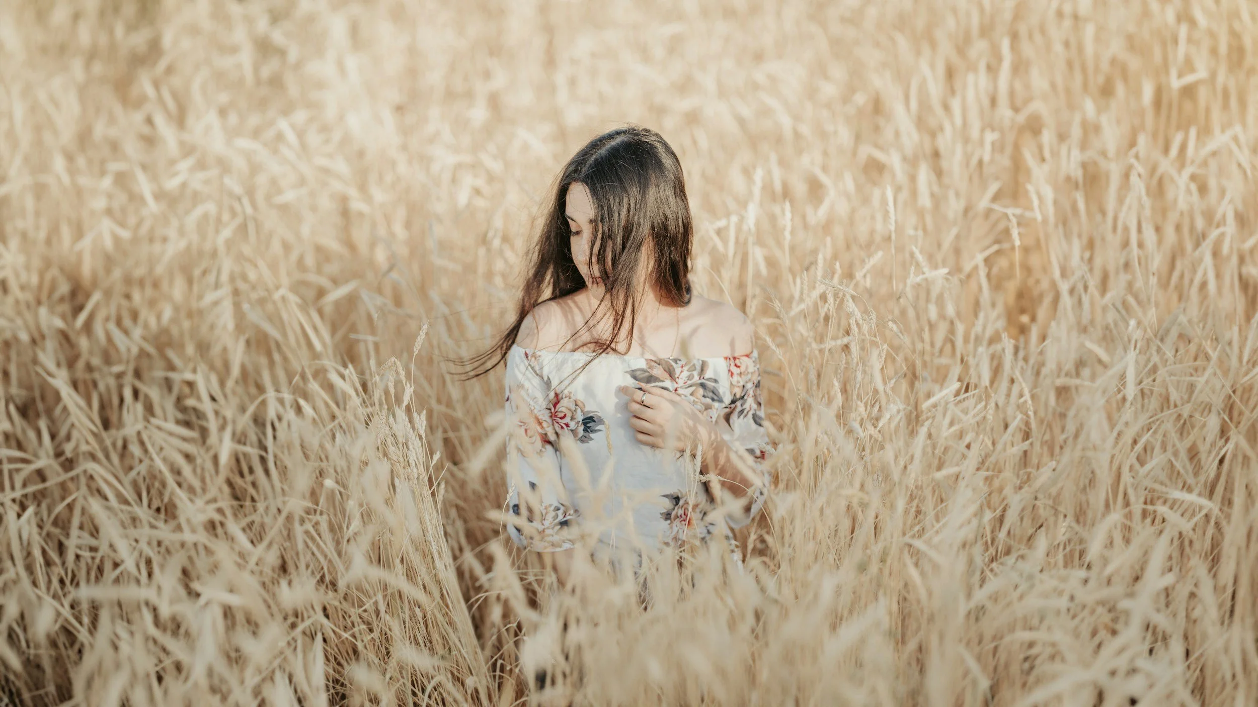 Woman in floral off-shoulder dress standing in a wheat field