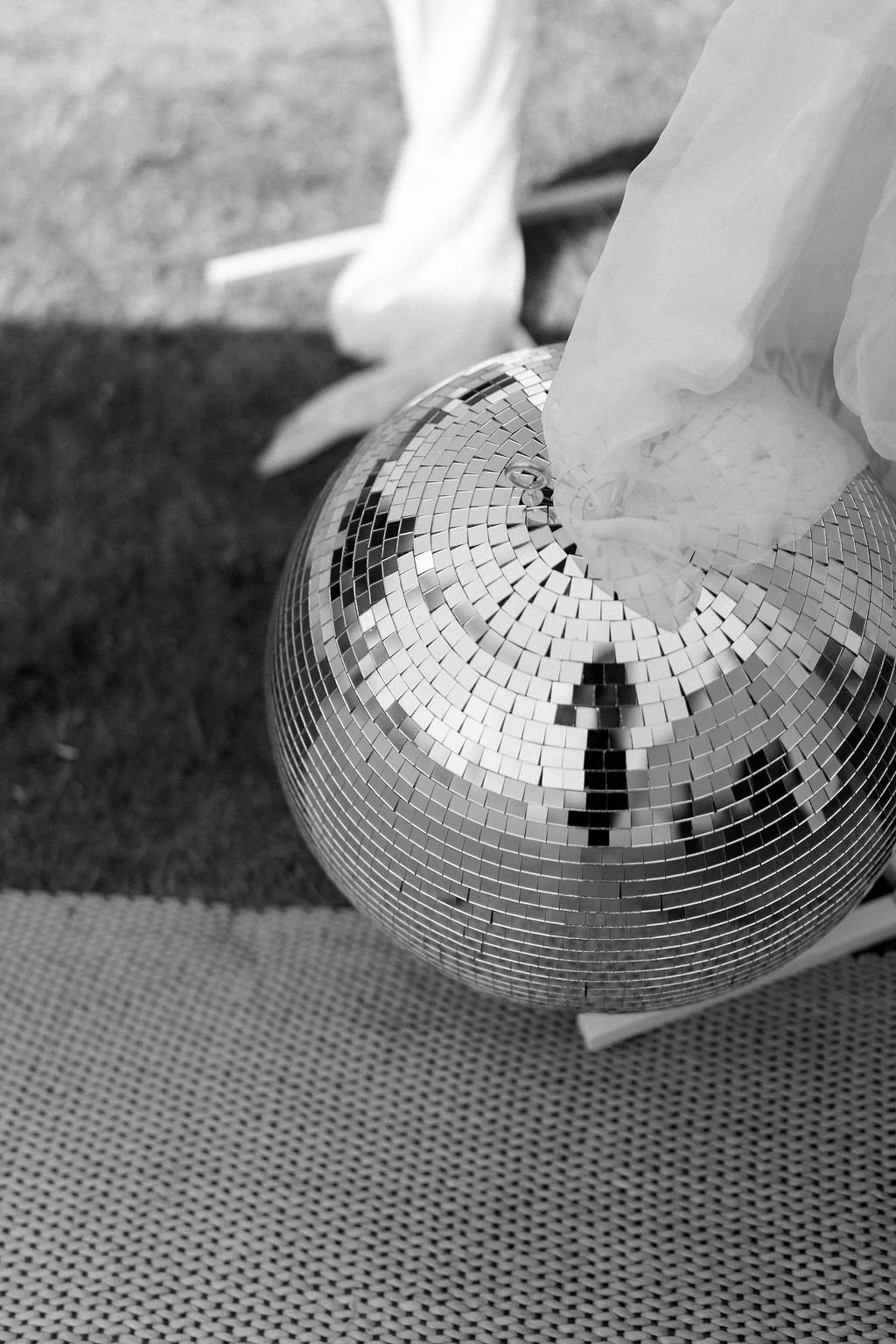 A spherical disco ball covered in small mirror tiles reflecting light and surroundings, resting on a textured surface.
