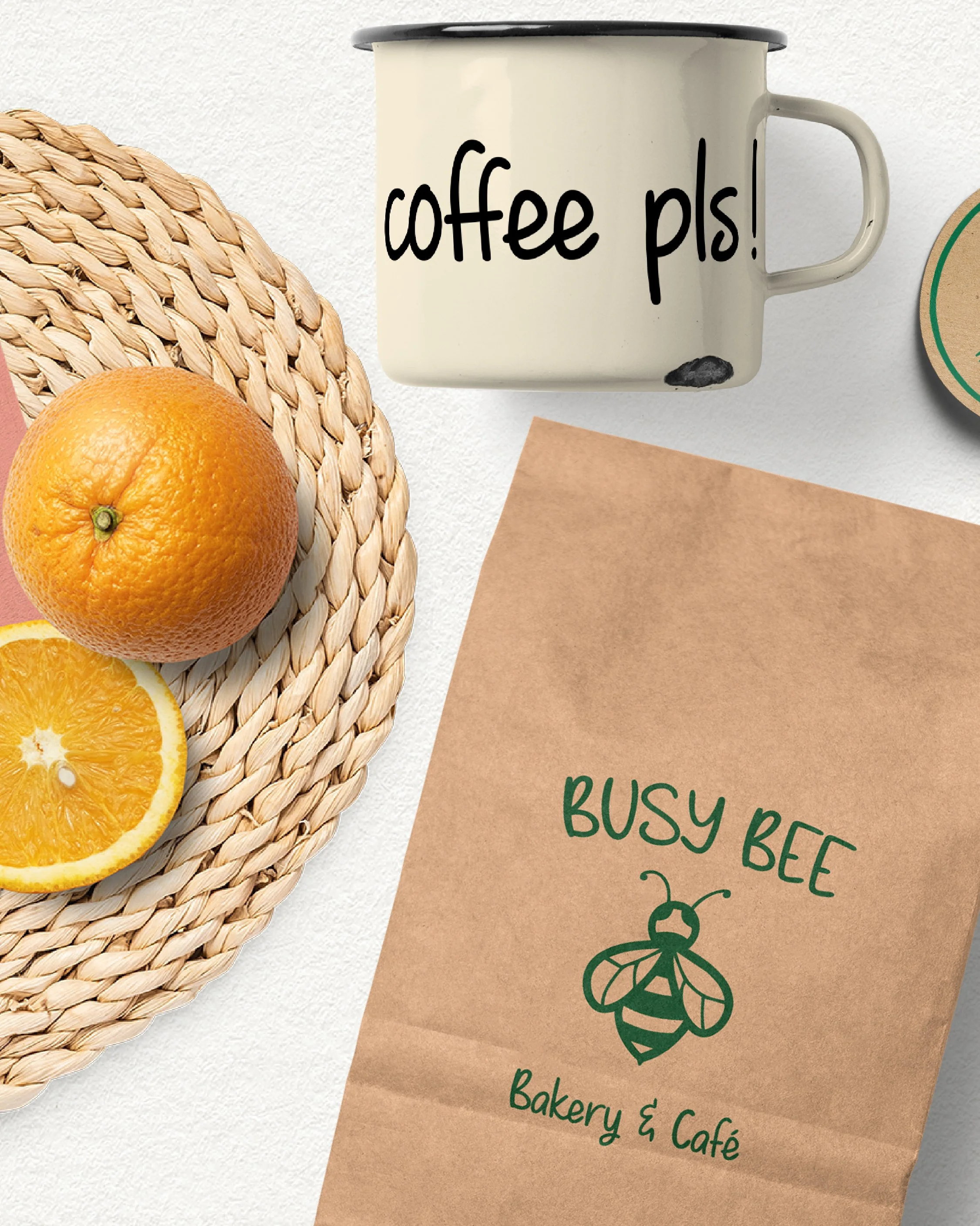 Top view of a woven straw placemat with halved oranges, a white enamel mug with black rim inscribed with "coffee pls!", and a brown paper card with green text that says "BUSY BEE Bakery & Café" and a drawing of a bee.