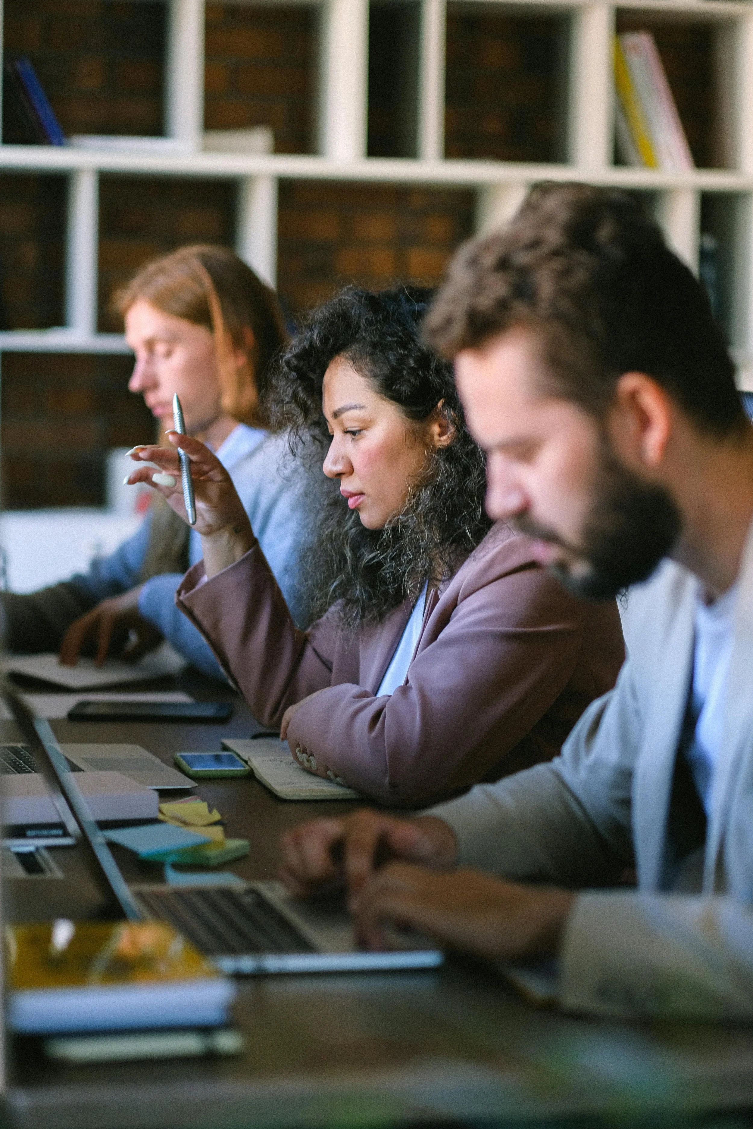 People working at a meeting table with laptops, notebooks, and sticky notes.