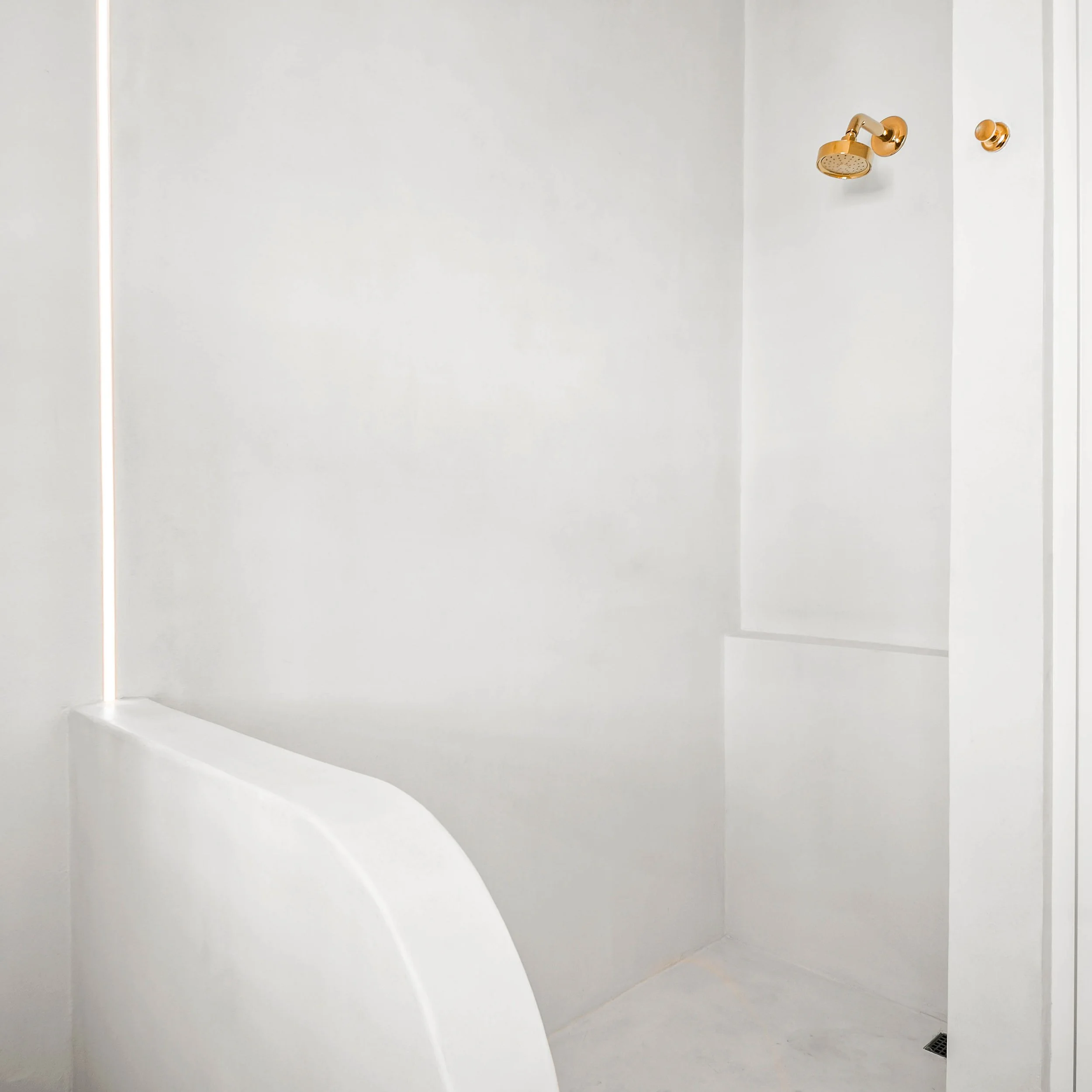 Minimalist Microcement Bathroom with Low Curved Pony Wall. Exposed Open Shower. LED Strip Bathroom Lighting. Marco Polo Lane Project, Cinnamon Shore North. Port Aransas, Texas - residential design by licensed architect Stefanie Mustian, Board and Bat