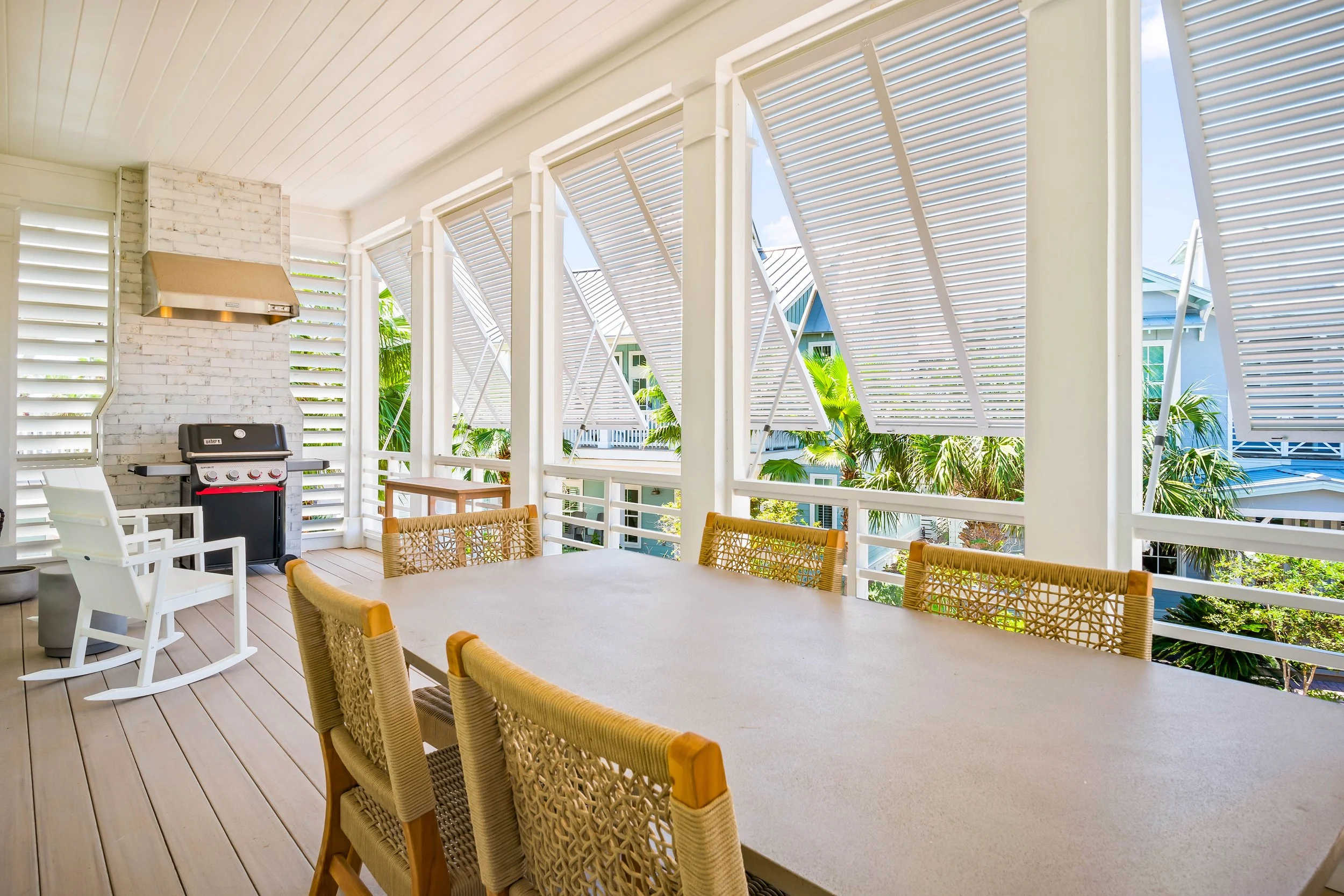 New Traditional Coastal Home Porch with Bahama Shutters, Concrete Dining Table and Outdoor Grill with Vent Hood. White Rocking Chairs. Marco Polo Lane Project, Cinnamon Shore North. Port Aransas, Texas - residential design by licensed architect Stefa