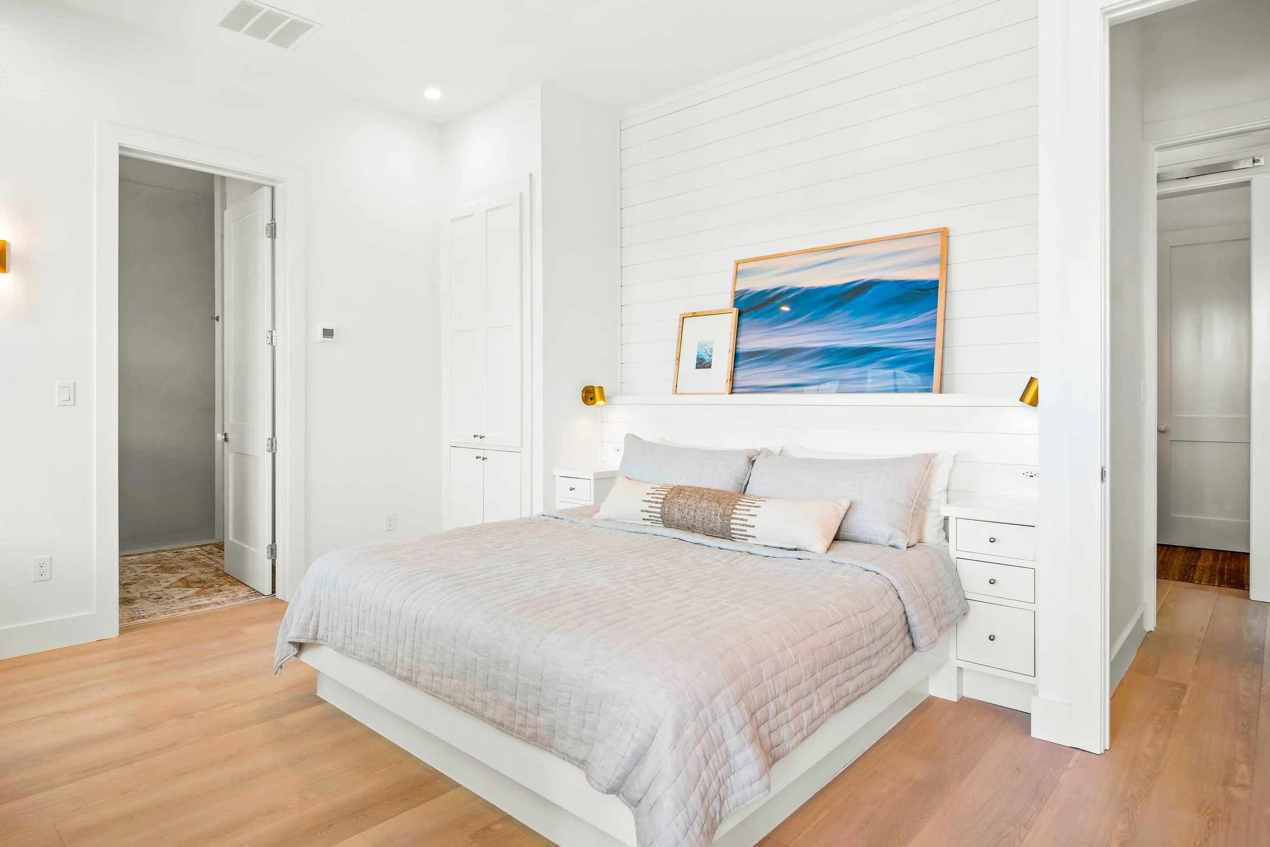 modern bedroom with gold sconces: Primary bedroom with custom lighting and artwork. Marco Polo Lane Project, Cinnamon Shore North. Port Aransas, Texas - residential design by licensed architect Stefanie Mustian, Board and Batten Architecture Design
