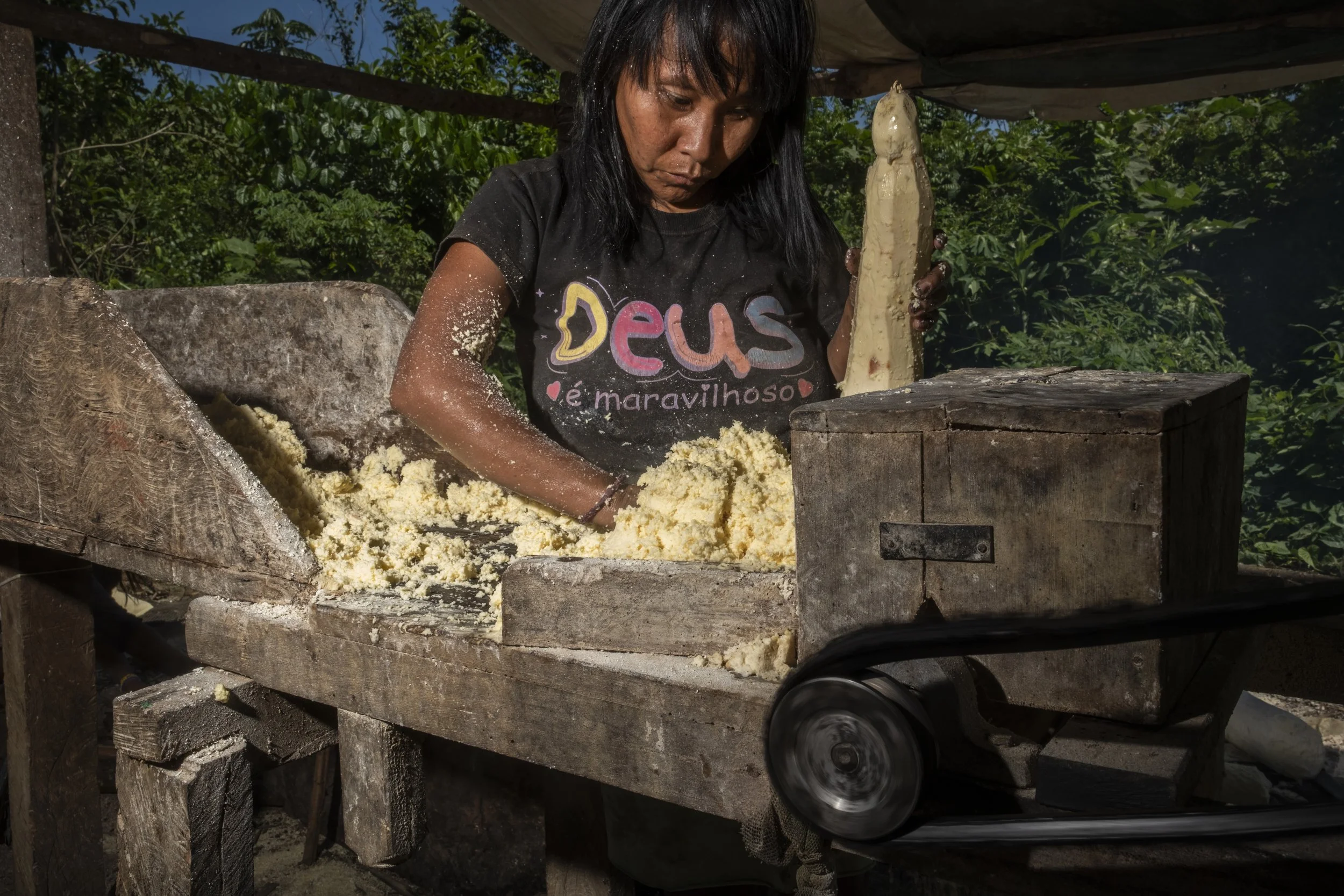 Na comunidade de Palimiu, uma mulher Yanomami utiliza uma máquina para moer mandioca, que depois é seca em cestos antes de ser cozida. A mandioca é um dos alimentos básicos nas aldeias Yanomami e sustenta grande parte da sua alimentação cotidiana.