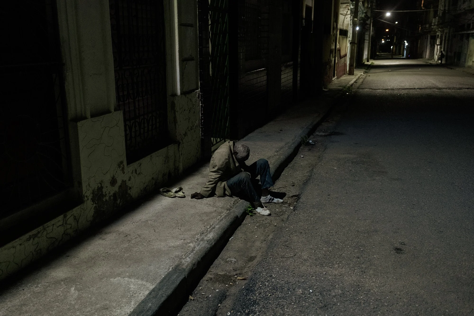 A drunk man lies nearly sprawled on a street in Havana at night.