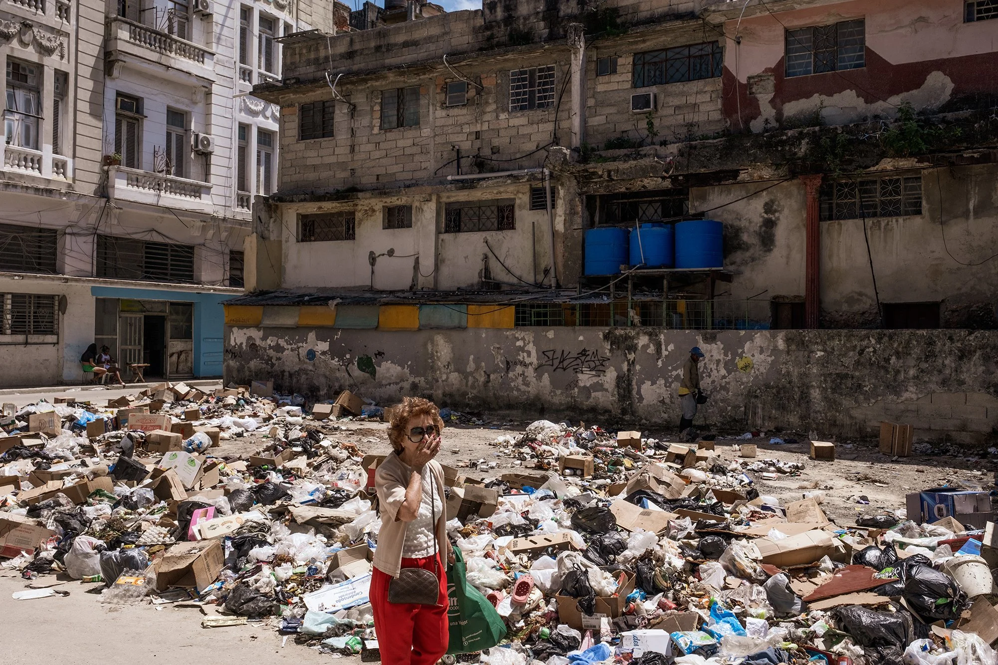 A woman covers her mouth as she walks past piles of uncollected garbage on a street in downtown Havana. 