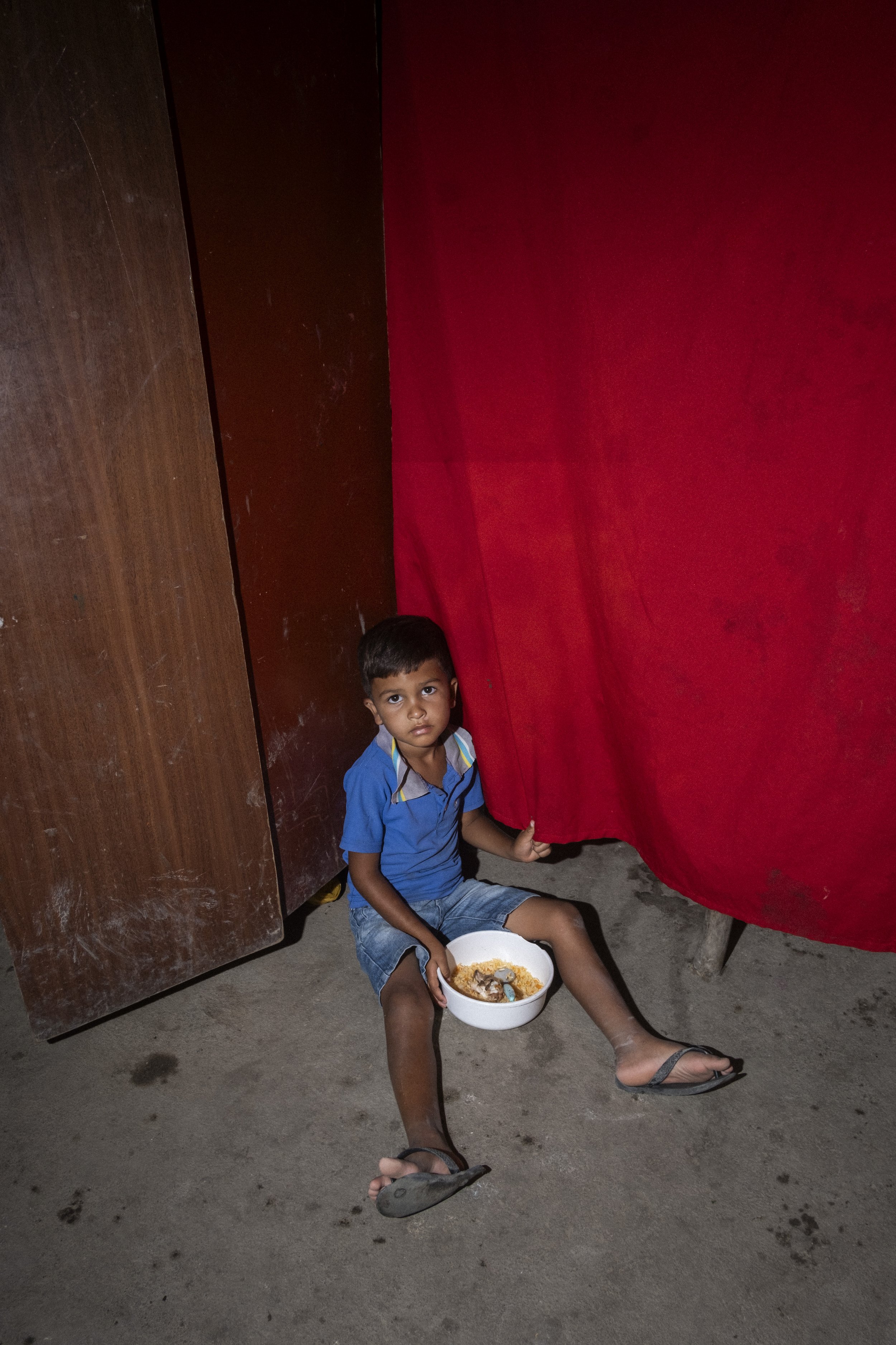 Uma criança almoça sentada no chão dentro de sua casa simples, em uma comunidade ocupada em Arapiraca, no interior rural do estado de Alagoas.