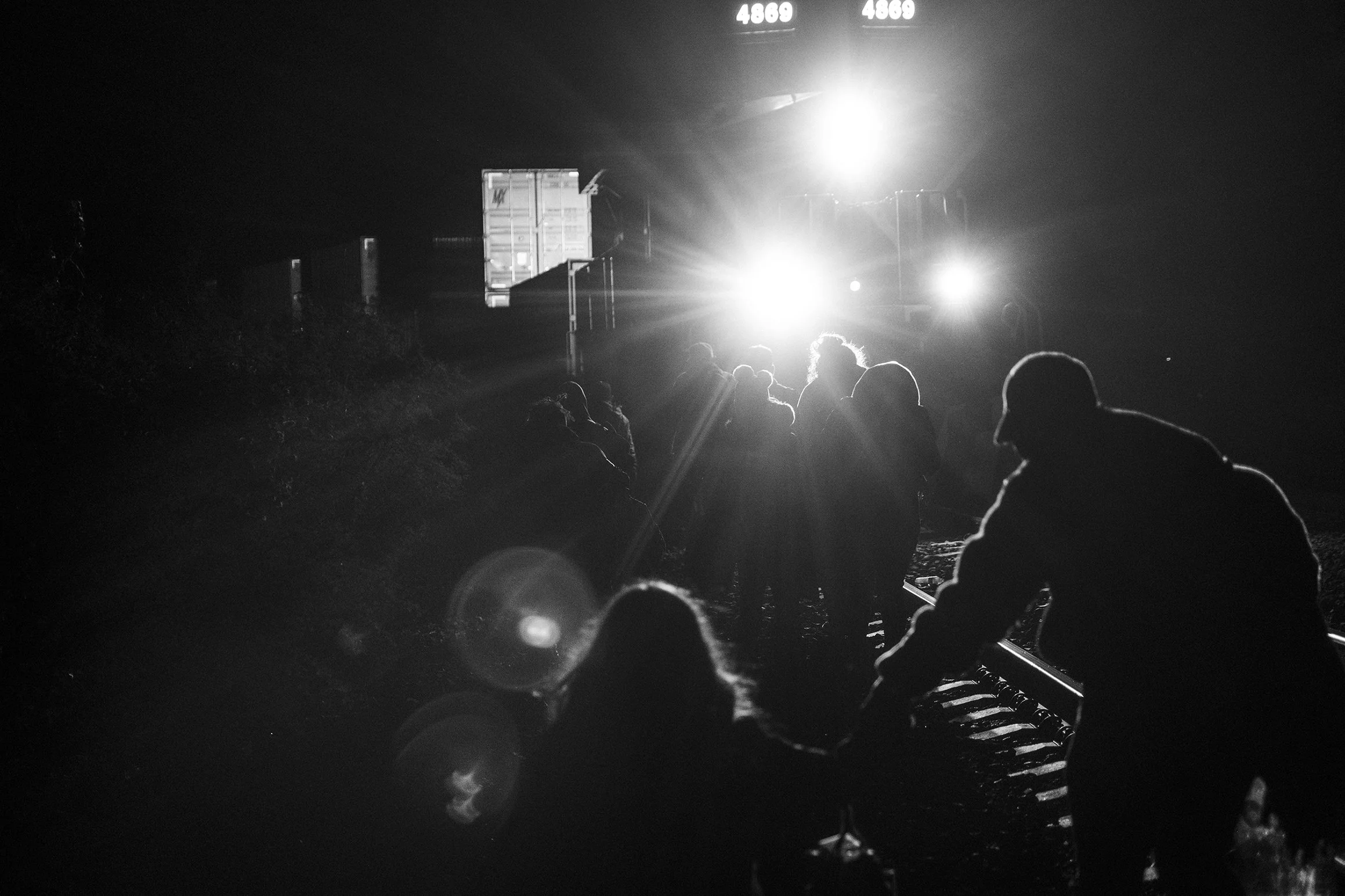 Cesar Atencio, his family, and a group of migrants rush along the railway tracks near San Francisco del Rincón, Mexico, as a freight train stops. They travel atop these trains, known as La Bestia, on their journey north.
