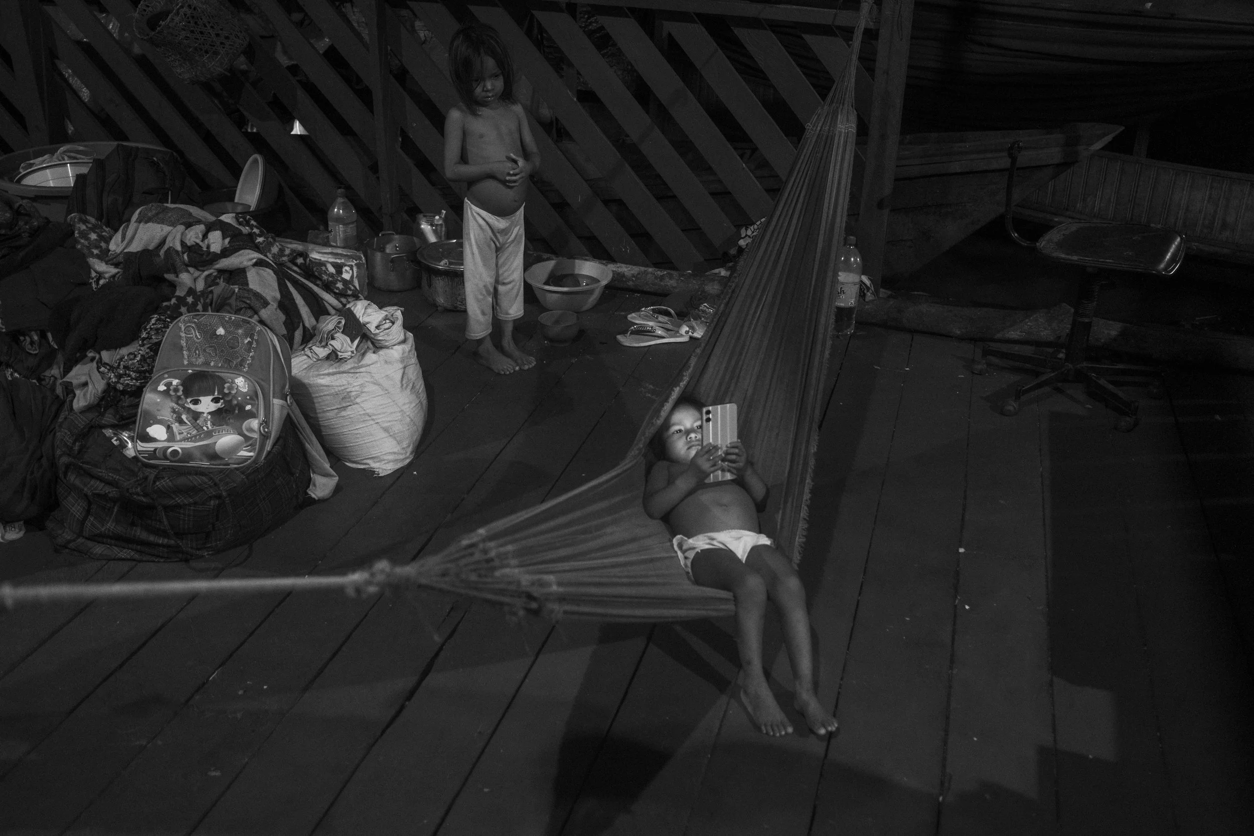 Kanamari children watch content on a smartphone inside a shelter in Atalaia do Norte, the main urban center and gateway to the Vale do Javari Indigenous Territory. Indigenous families regularly travel to the town to access healthcare, buy food, and r