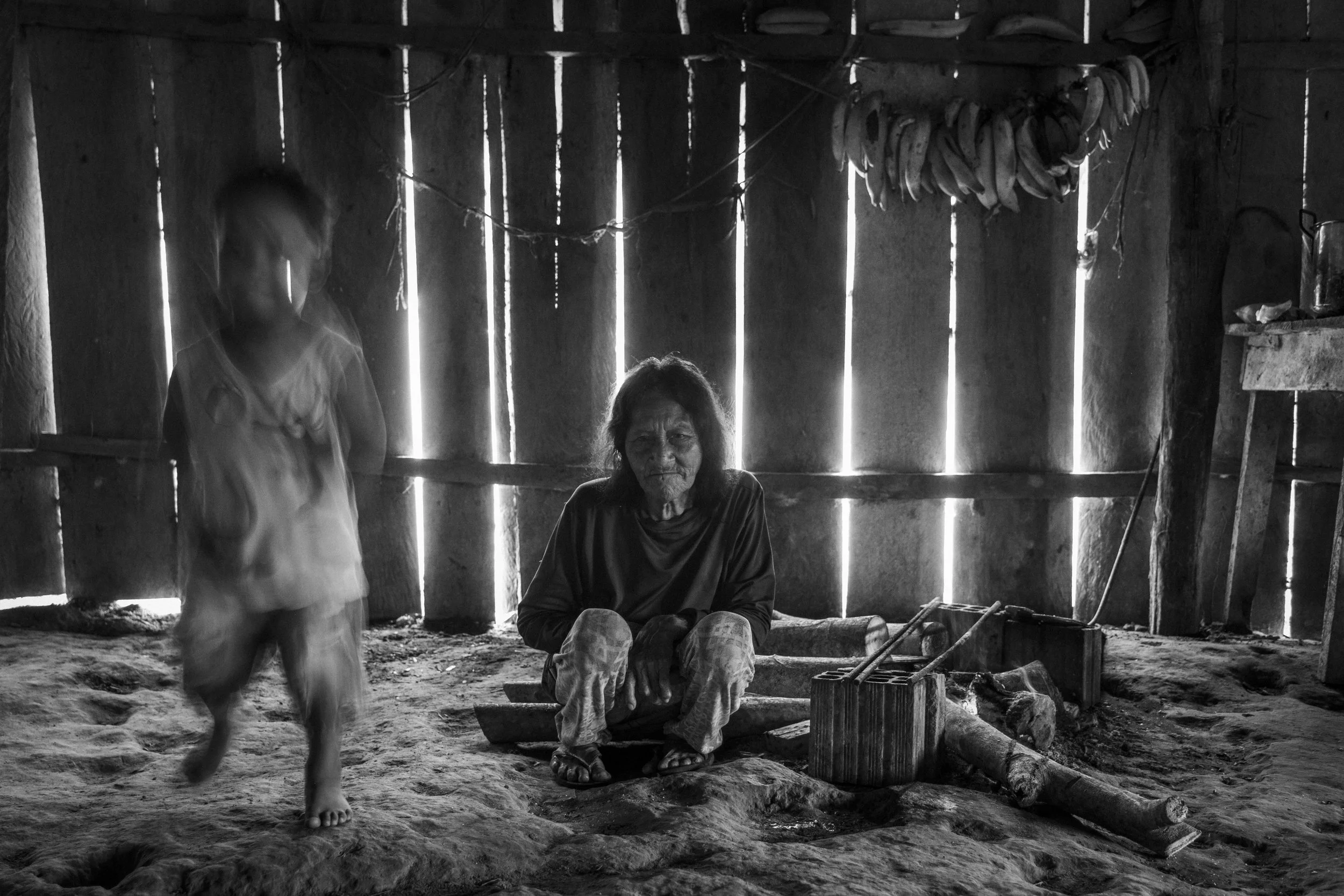 An elderly Mayoruna woman looks on as a child dances inside a communal house in Flores village, within the Vale do Javari Indigenous Territory, Brazil.
